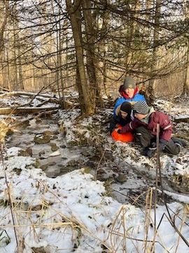 Children in the snow playing by stream