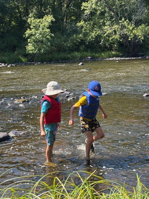 A group of people walking along a river near trees
