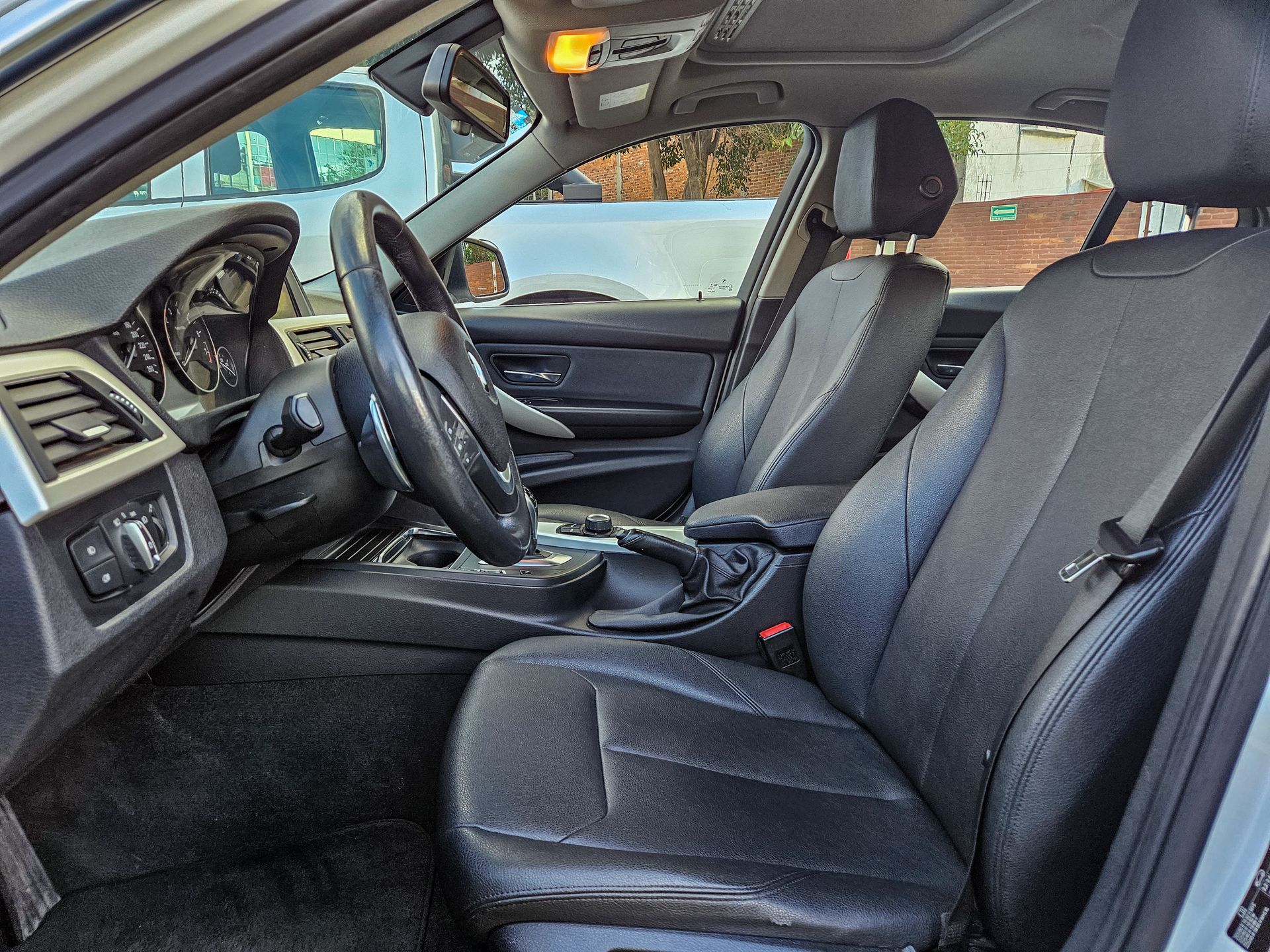 Interior de cuero negro de un automóvil, con el asiento del conductor, el volante y el tablero visibles.