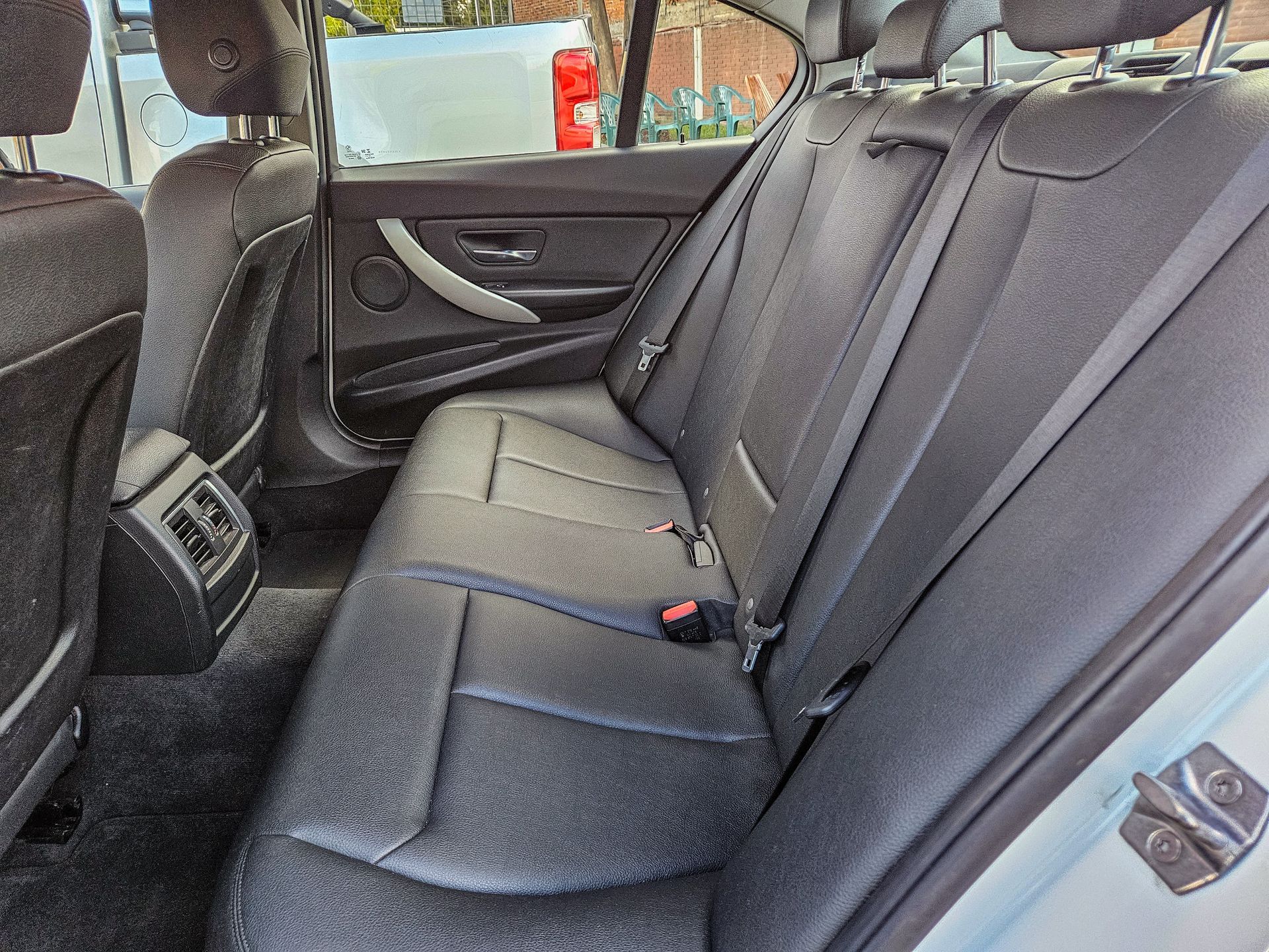 Vista interior de los asientos traseros de un automóvil; se ven asientos de cuero negro, reposacabezas y salidas de aire.