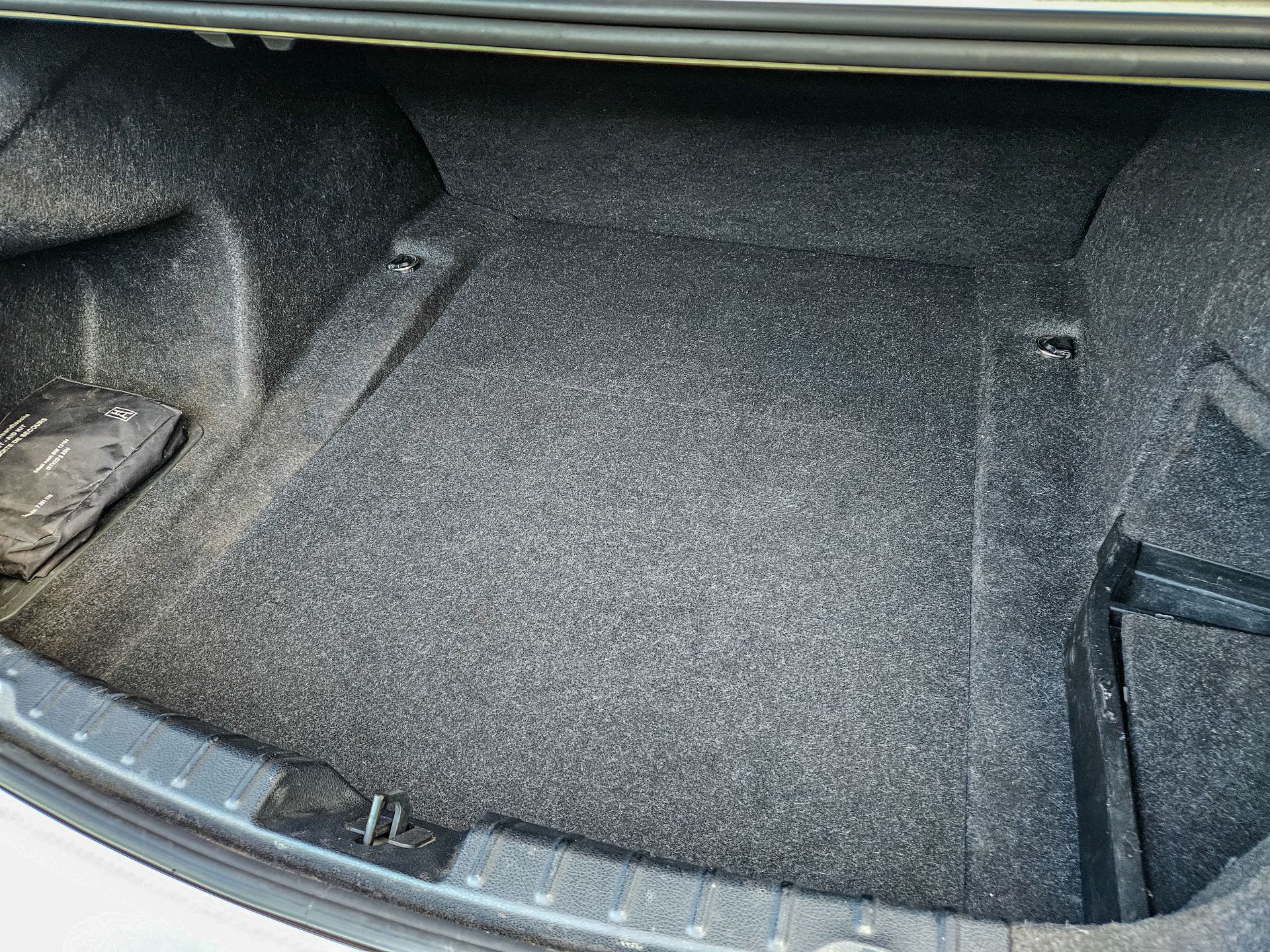 Interior de maletero de coche con alfombra gris y compartimentos de almacenamiento.