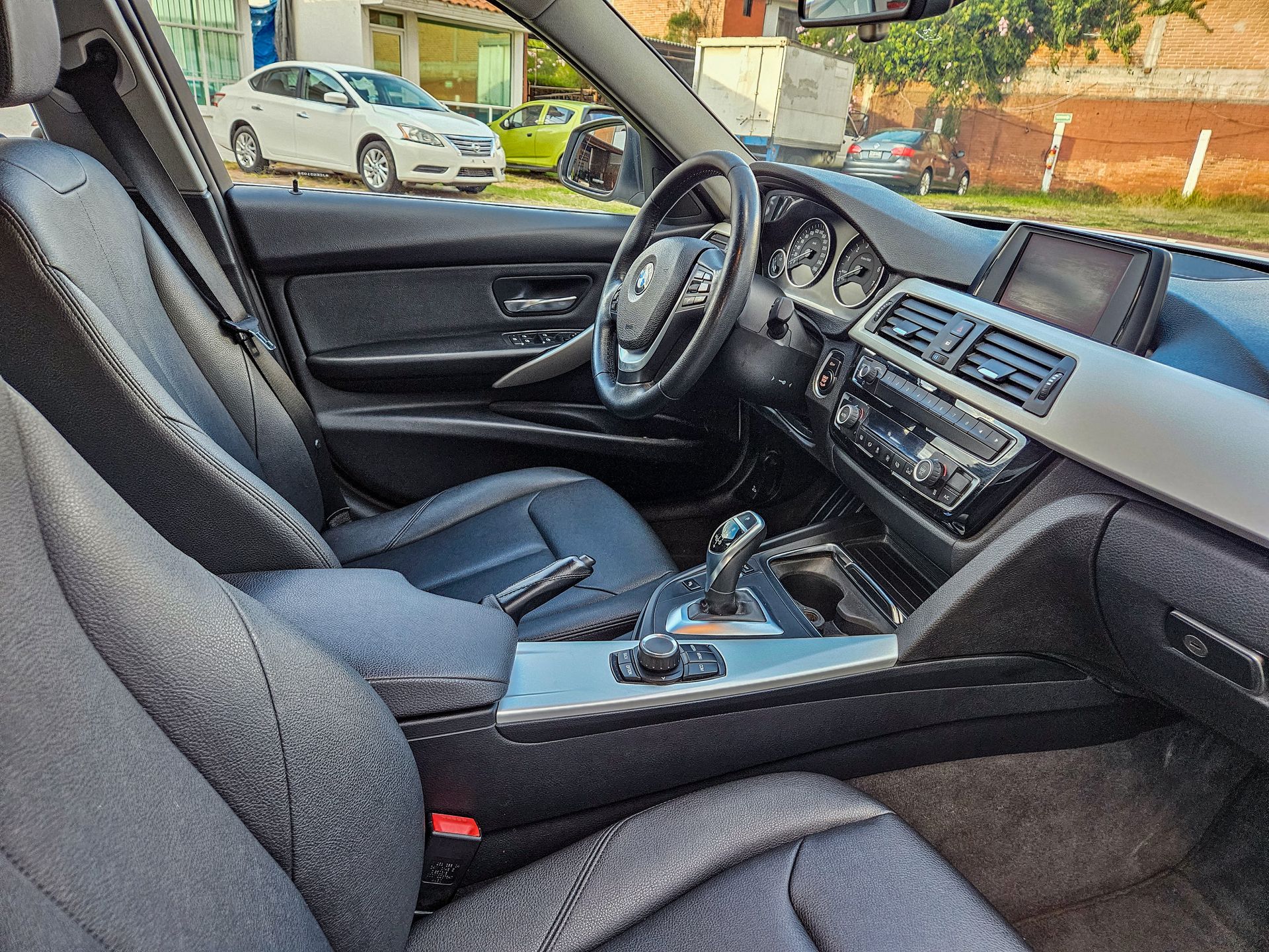 Interior de un automóvil BMW negro con volante, tablero, asientos y consola central visibles.