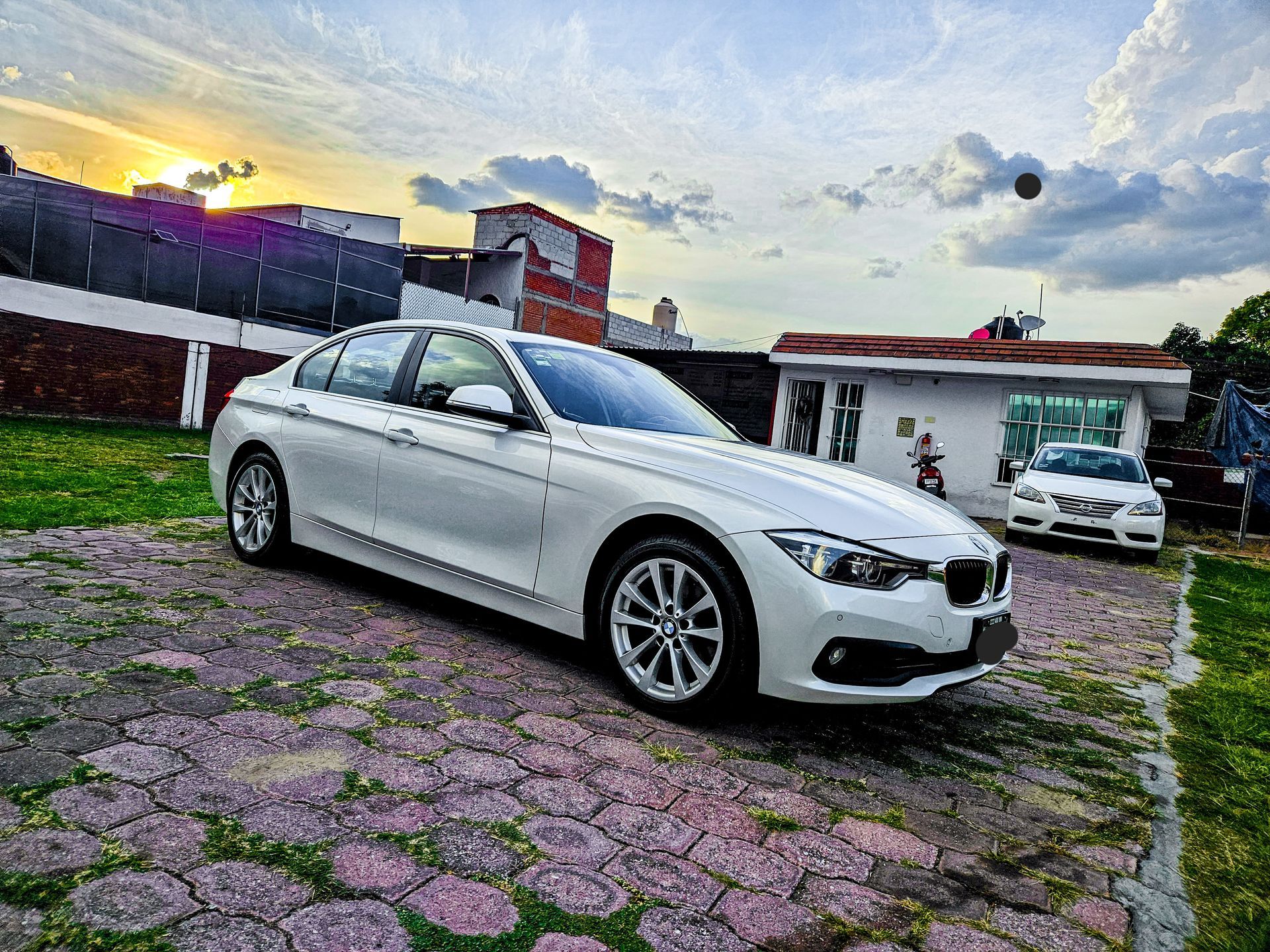 Un BMW sedán blanco estacionado sobre adoquines con un pequeño edificio al fondo.