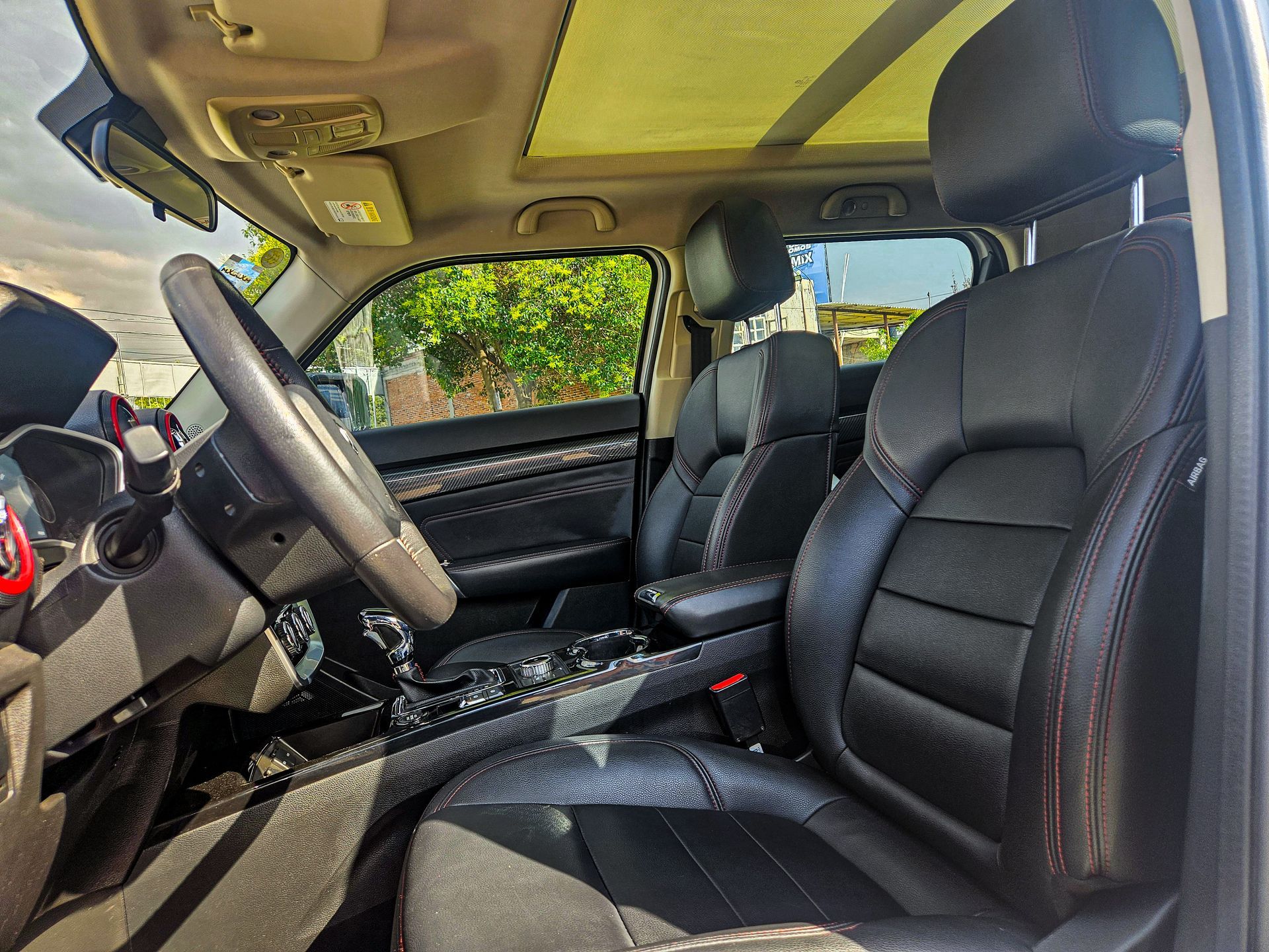 Interior de un automóvil con asientos de cuero negro, volante y techo corredizo.