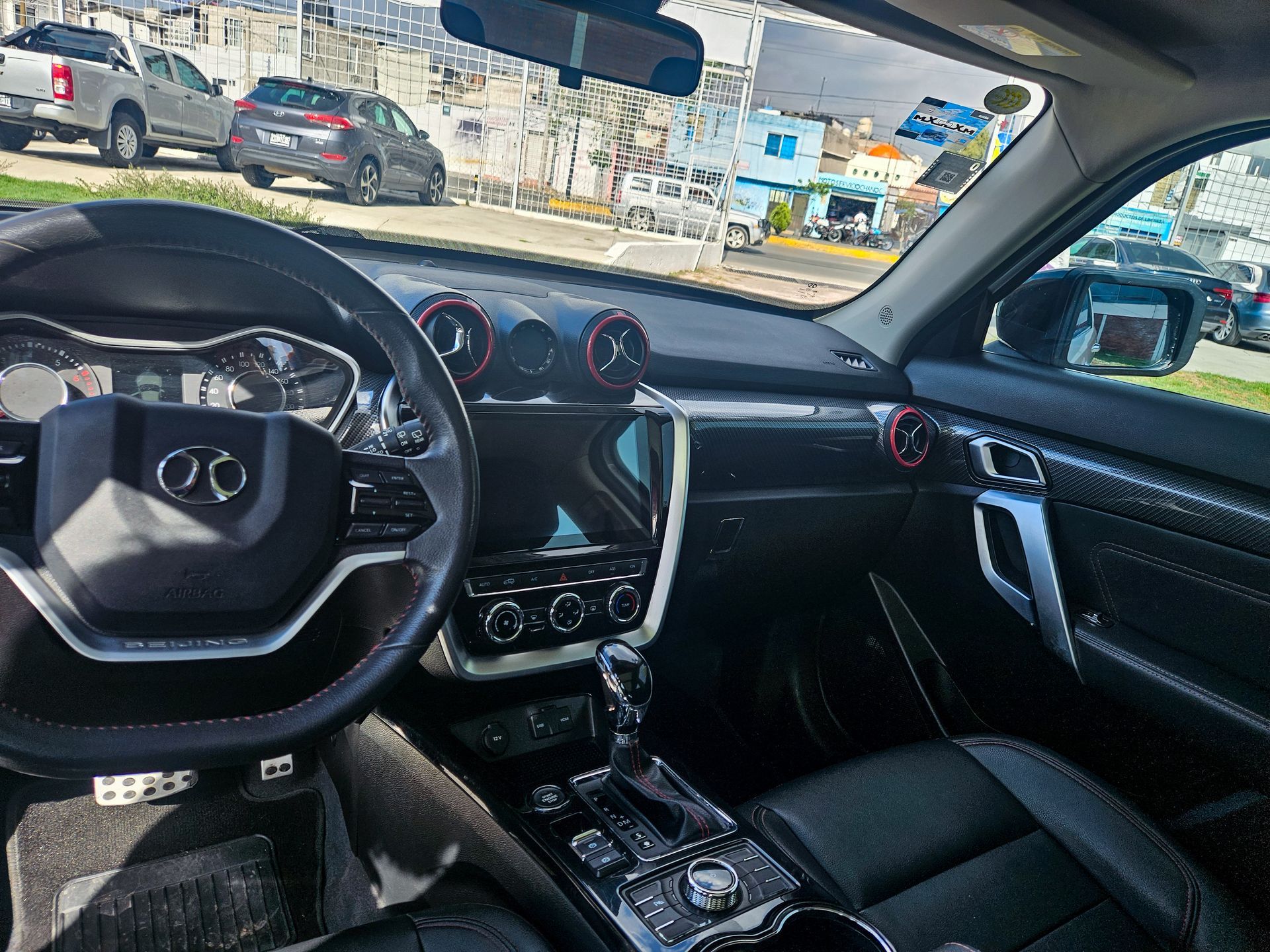 Vista interior del salpicadero y el asiento delantero de un coche. Se aprecian asientos de cuero negro, detalles plateados y un volante.