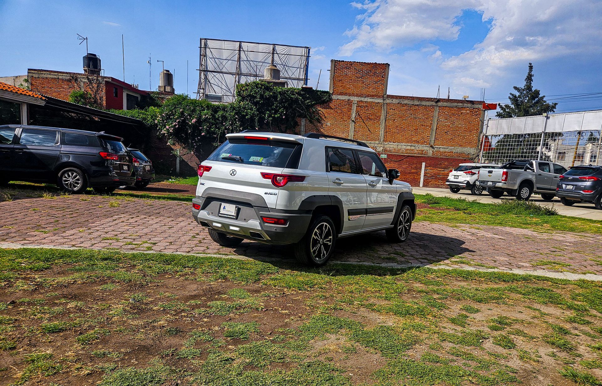 SUV plateado estacionado sobre grava con otros vehículos en un estacionamiento al aire libre.