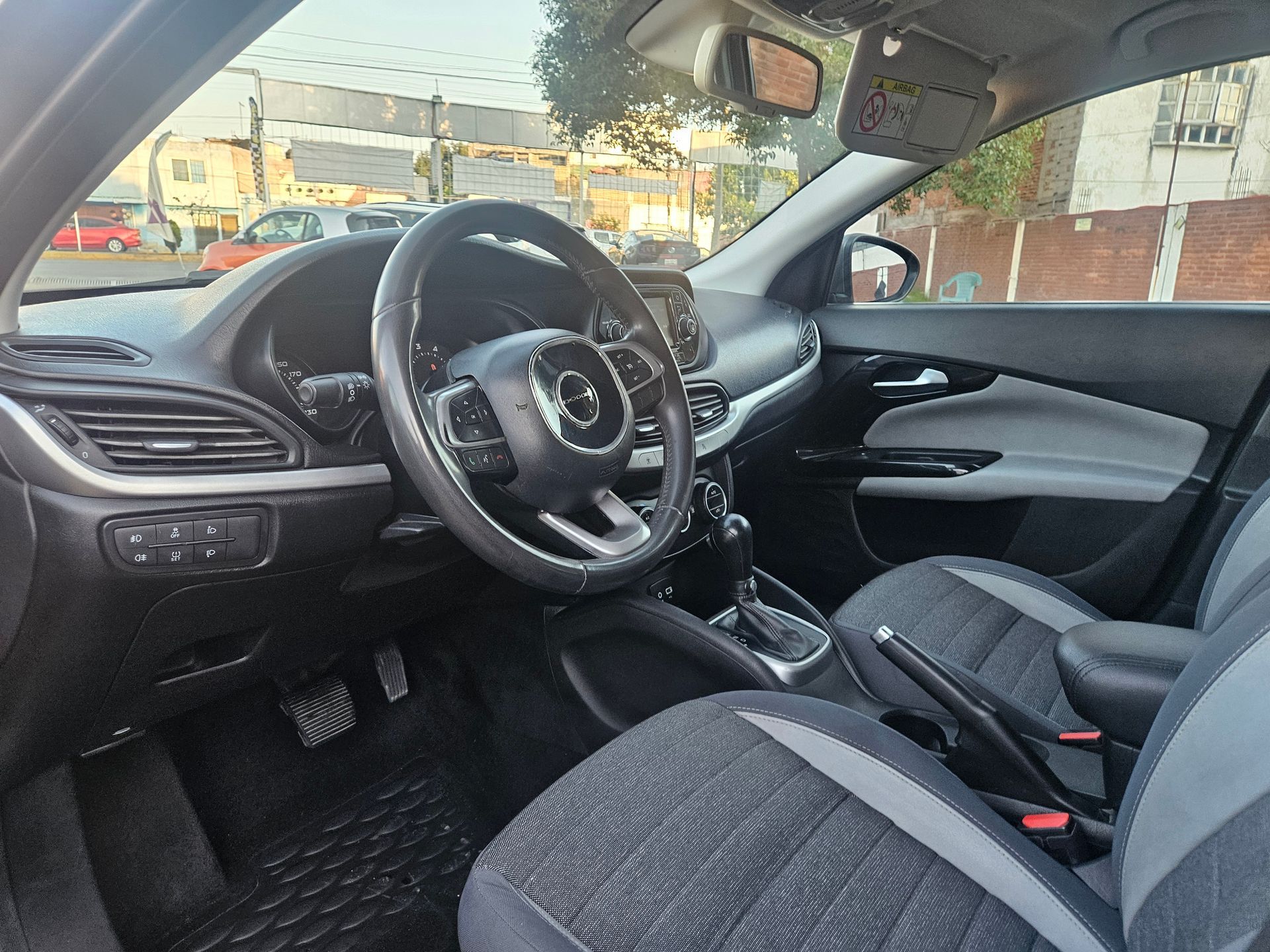 Interior de un automóvil con volante negro, asientos grises y tablero negro.