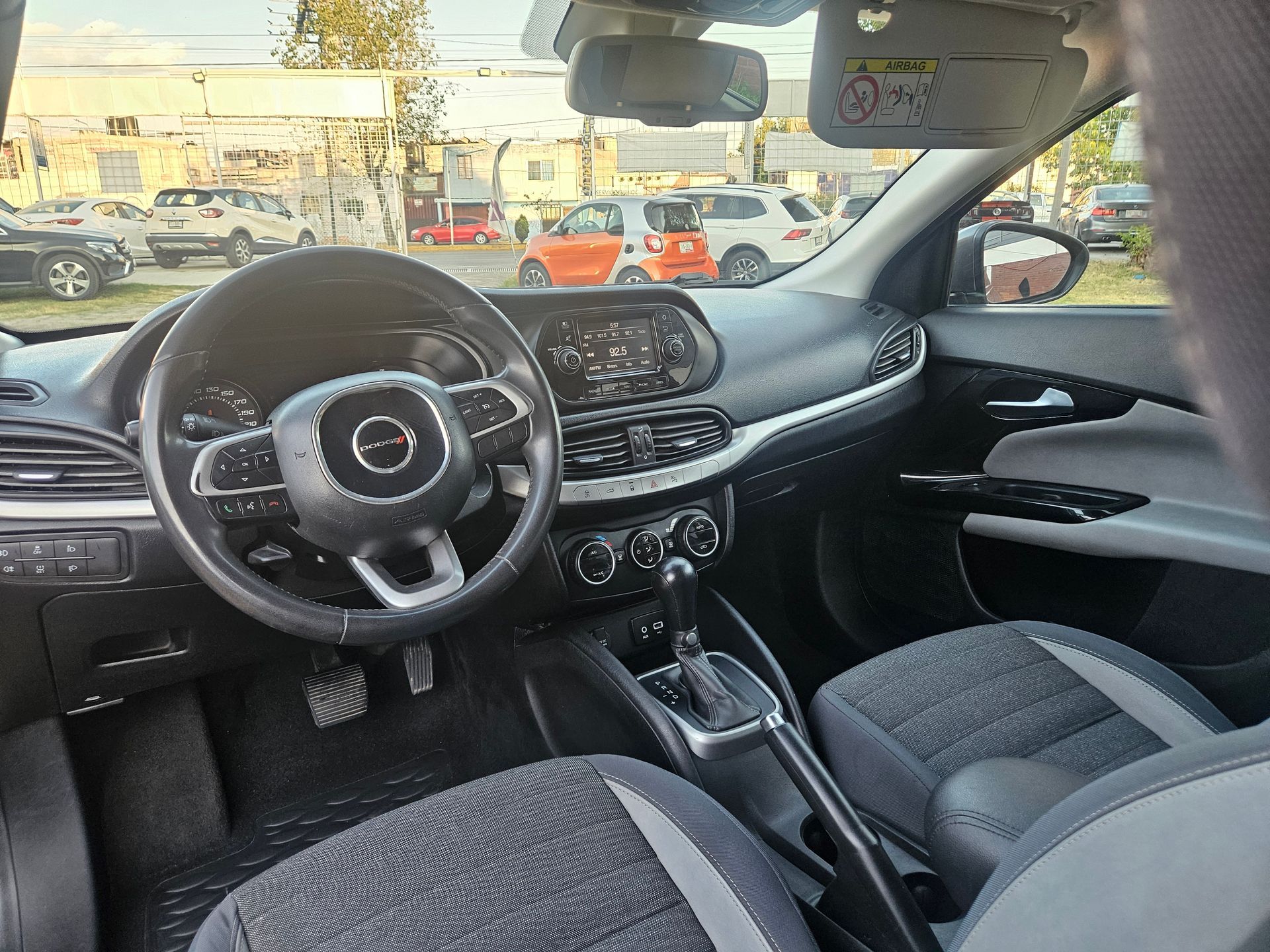 Interior de un automóvil con tablero negro, volante y asientos grises.