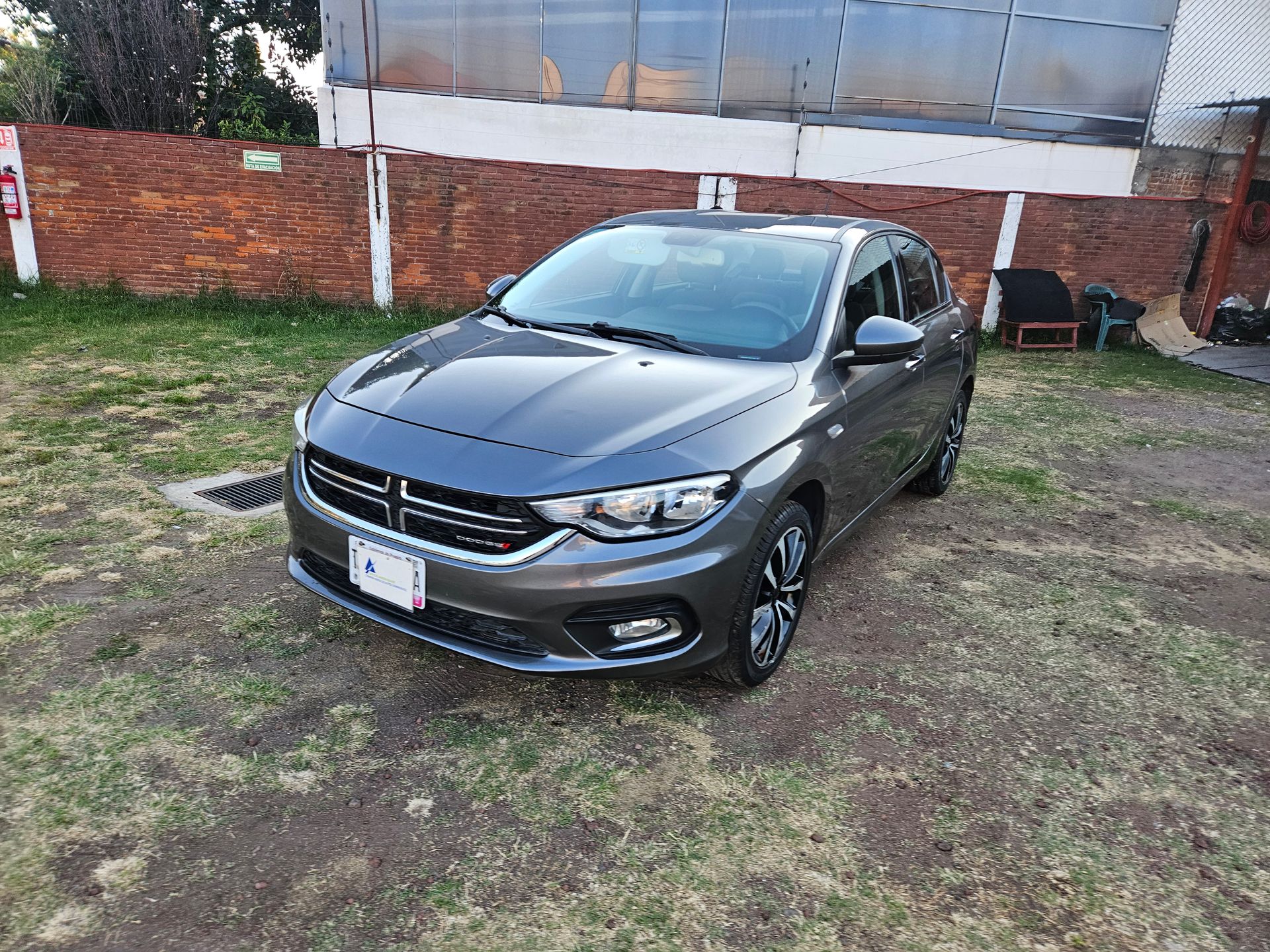 Dodge Neon gris estacionado en el césped frente a un edificio.