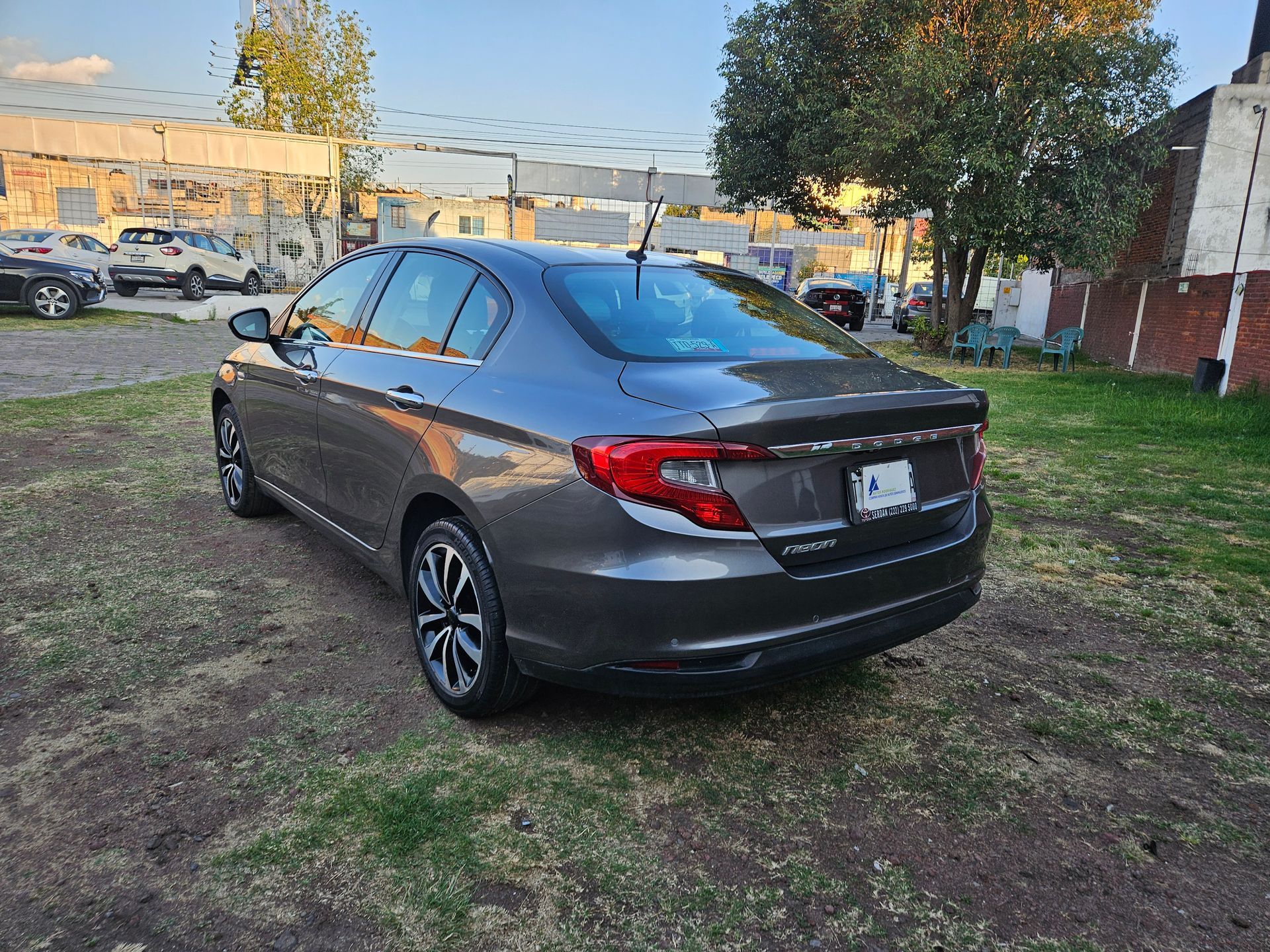 Sedán gris oscuro estacionado sobre el césped, con edificios al fondo.