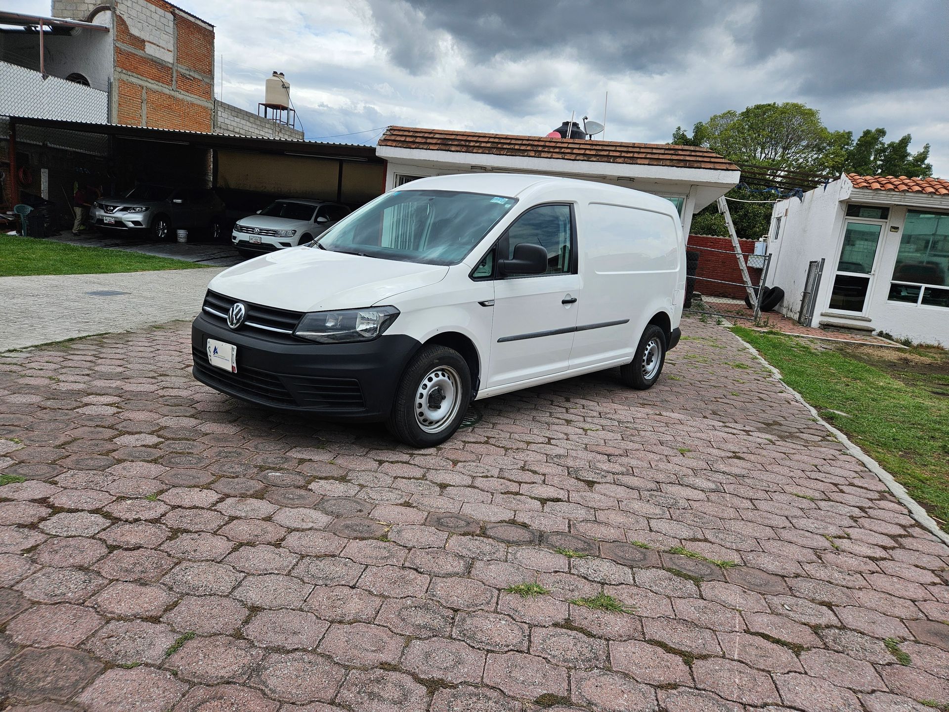 Furgoneta de carga Volkswagen Caddy blanca estacionada en un camino adoquinado bajo un cielo nublado.