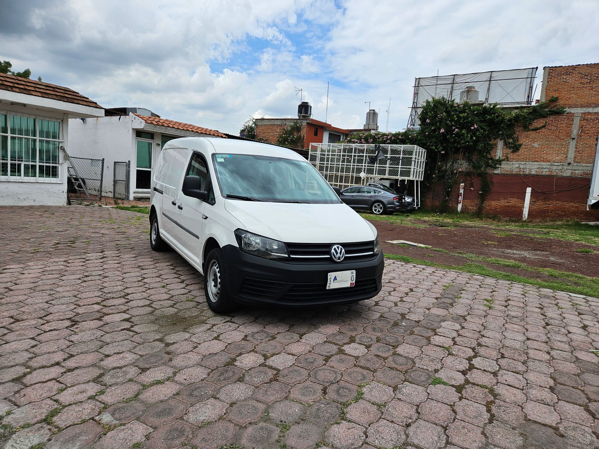 Furgoneta Volkswagen Caddy blanca estacionada sobre adoquines; entorno residencial con cielo nublado.