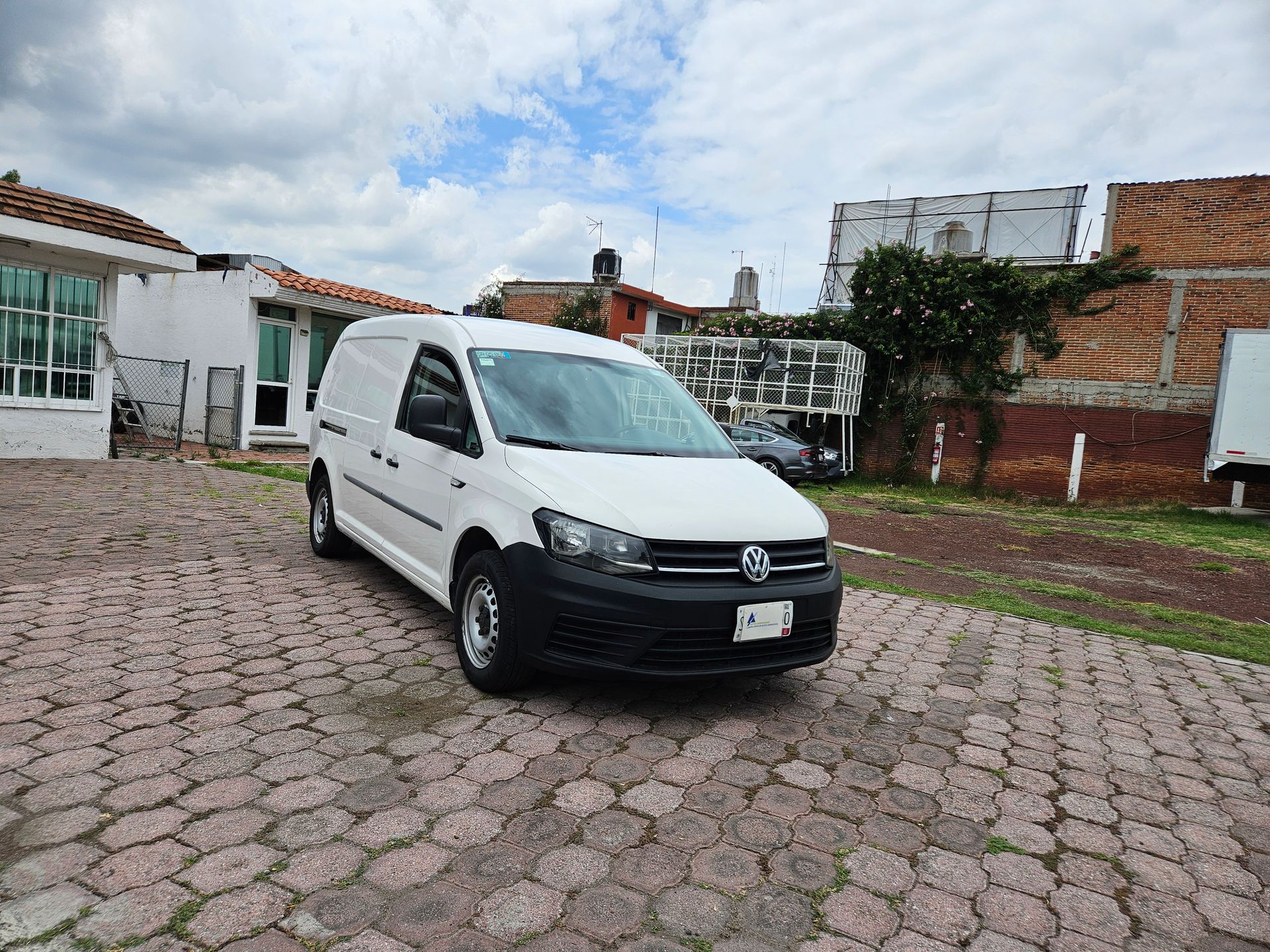 Furgoneta Volkswagen Caddy blanca estacionada sobre adoquines. Cielo nublado y edificios al fondo.