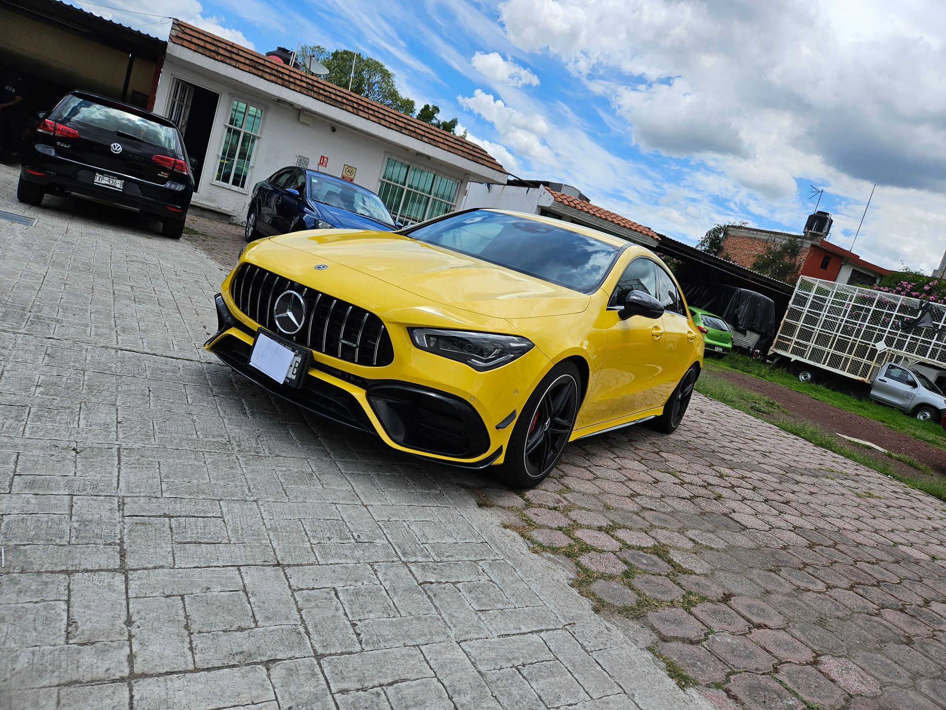 Un Mercedes-Benz CLA amarillo estacionado en un camino adoquinado bajo un cielo nublado.