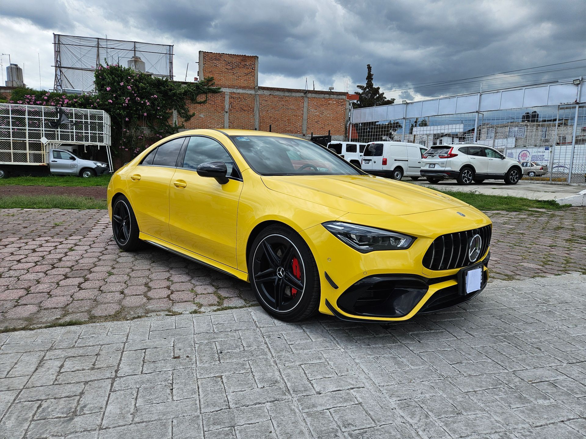 Mercedes-AMG CLA amarillo estacionado en un terreno pavimentado con un cielo nublado de fondo.