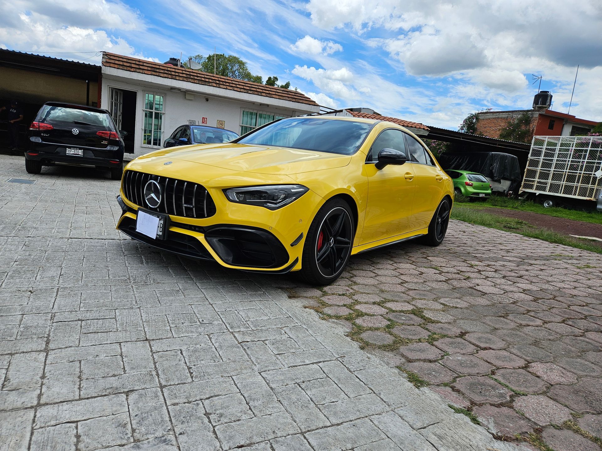 Un Mercedes-Benz CLA amarillo estacionado en un camino adoquinado bajo un cielo nublado.