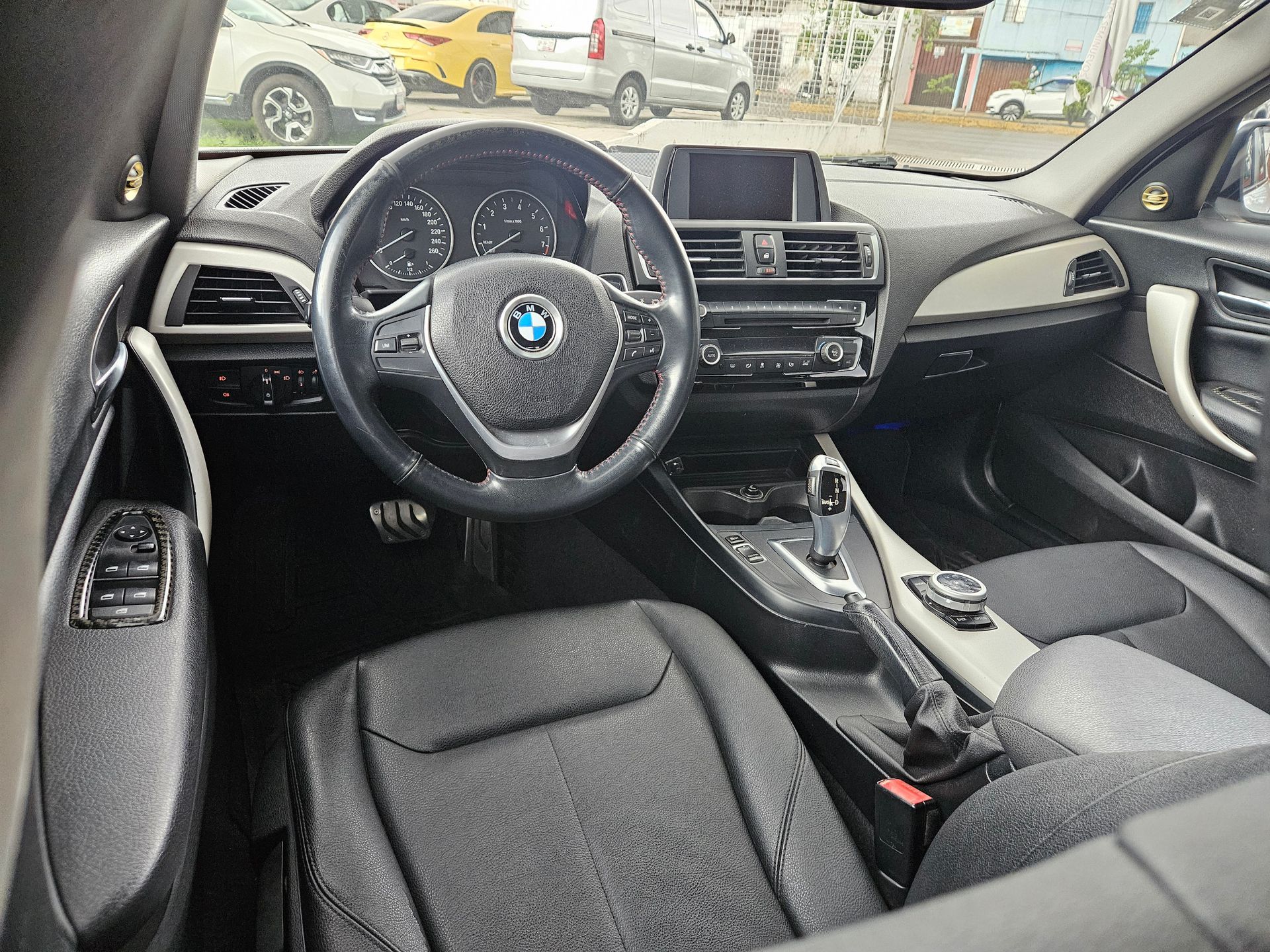Interior de un automóvil BMW negro con volante, tablero, asientos y consola visibles.