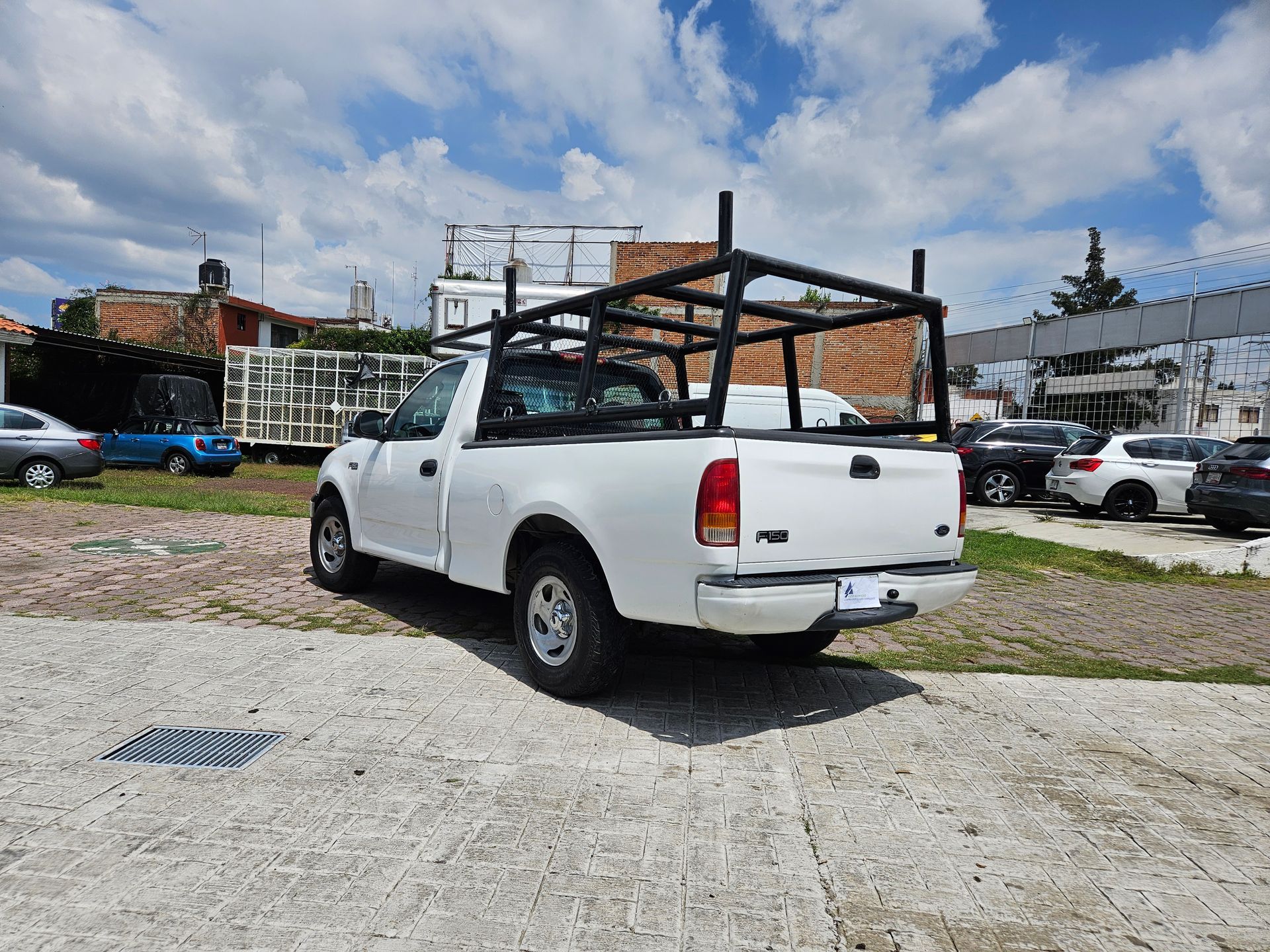 Camioneta blanca con parrilla negra estacionada sobre pavimento, fondo de cielo azul.