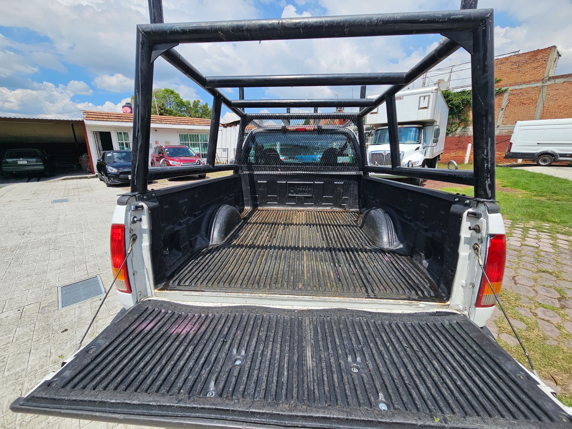 Caja de camioneta blanca con estructura de metal negro, portón trasero bajado, entorno exterior soleado.