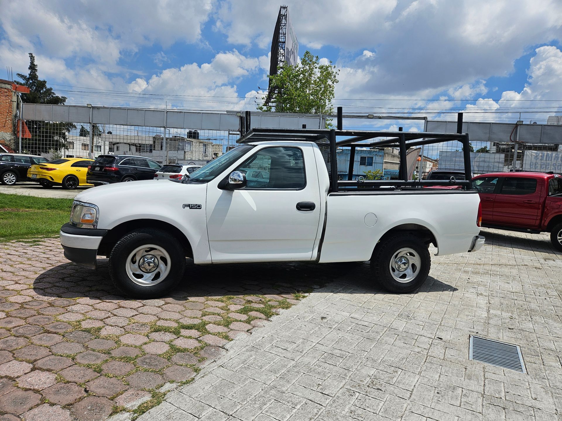 Camioneta Ford F-150 blanca con portaequipaje negro estacionada en un lote pavimentado en un día soleado.