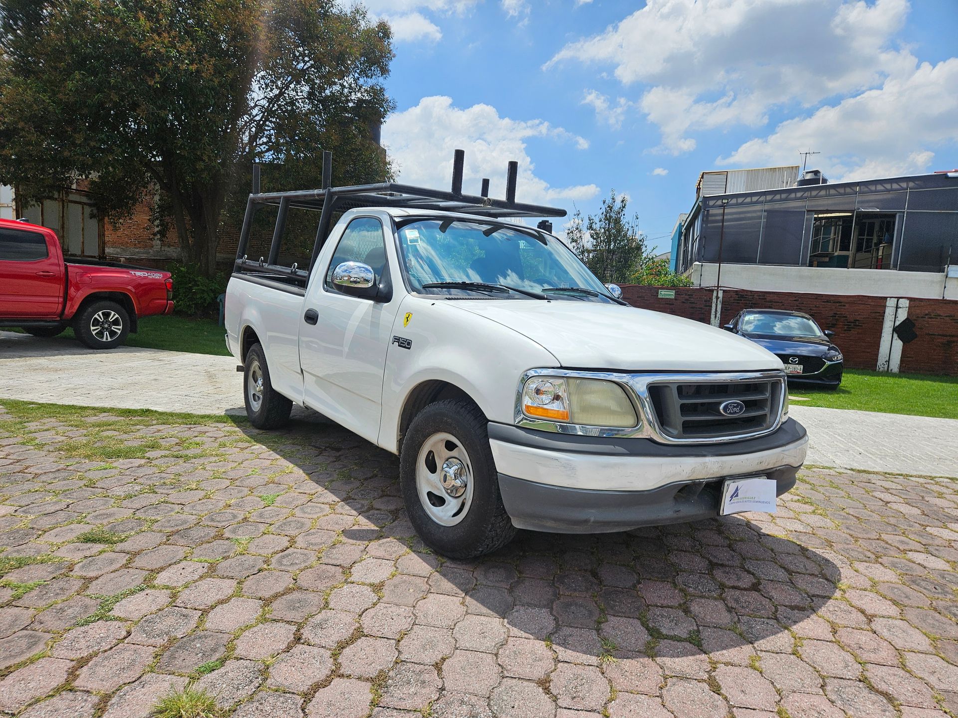 Camioneta Ford blanca con carrocería tipo camping negra estacionada sobre adoquines.