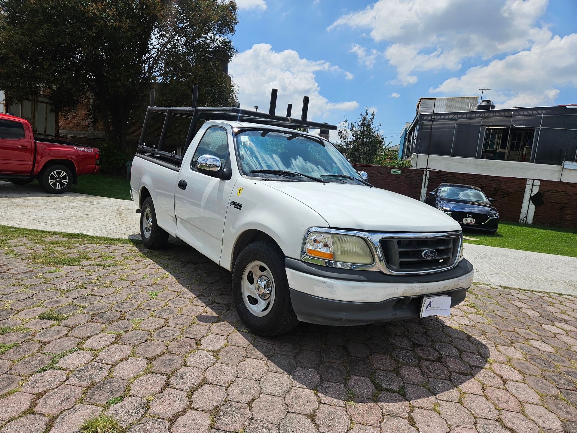 Camioneta Ford blanca con parrilla negra, estacionada sobre adoquines.