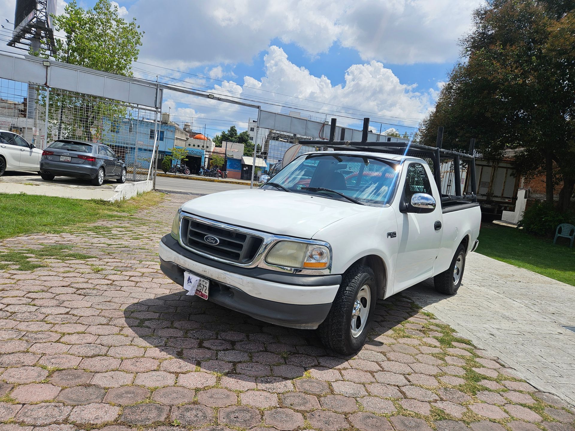 Camioneta Ford F-150 blanca estacionada en un camino pavimentado frente a un edificio en un día soleado.