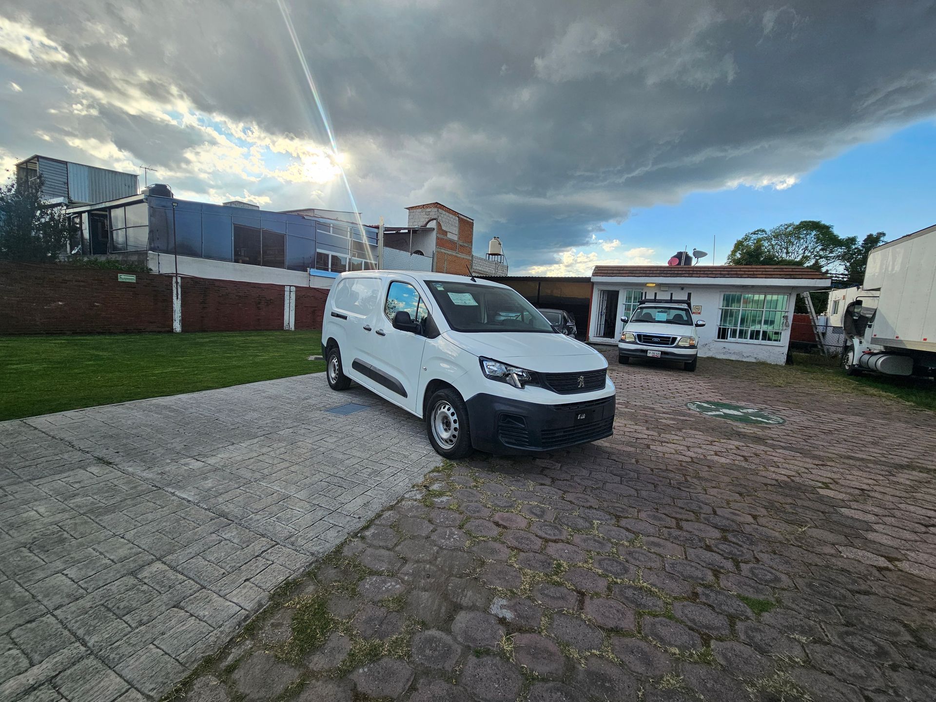 Furgoneta de carga blanca estacionada sobre adoquines; cielo nublado.