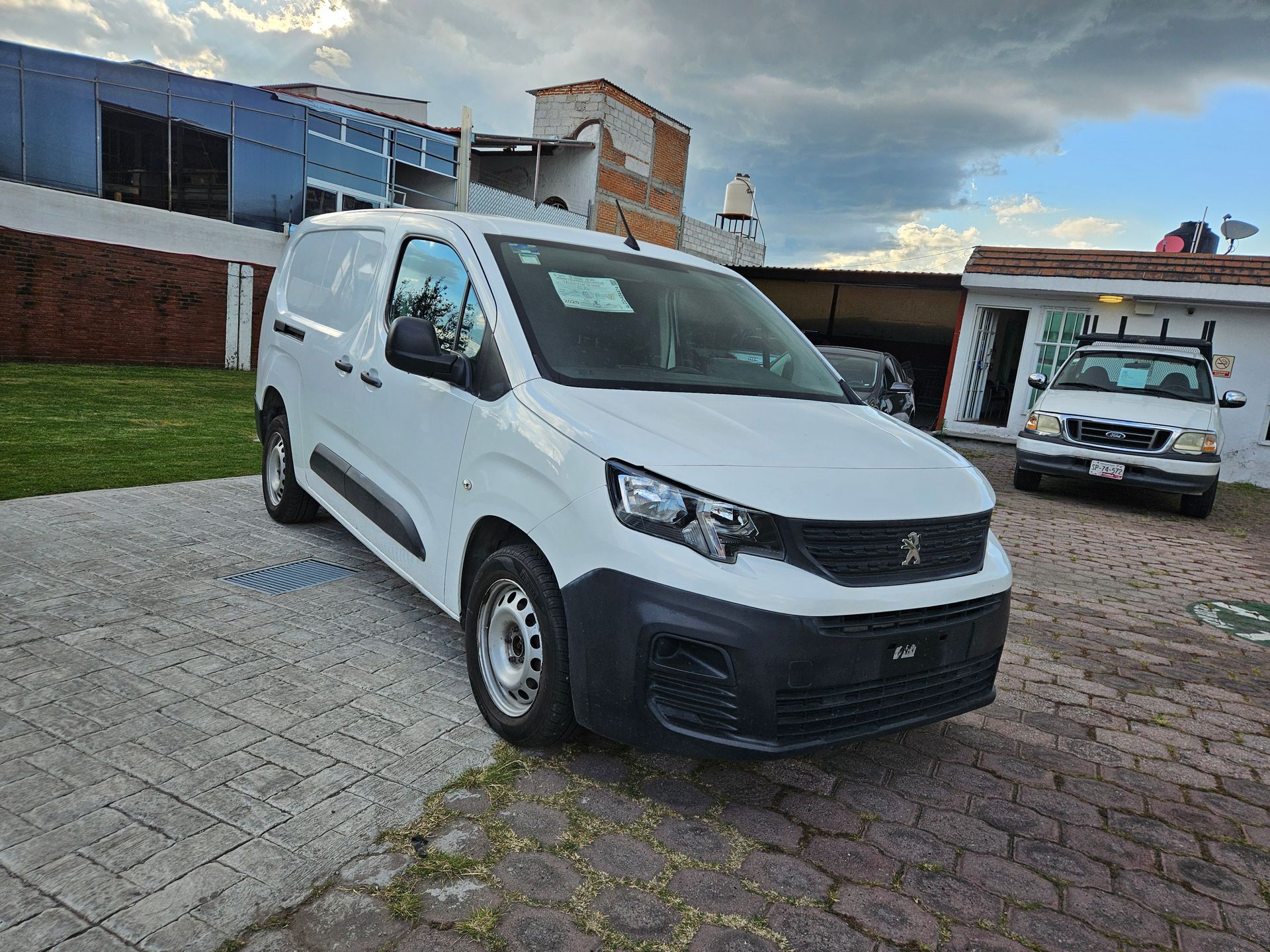 Furgoneta Peugeot Partner de color blanco estacionada al aire libre en una zona asfaltada, con cielo nublado al fondo.