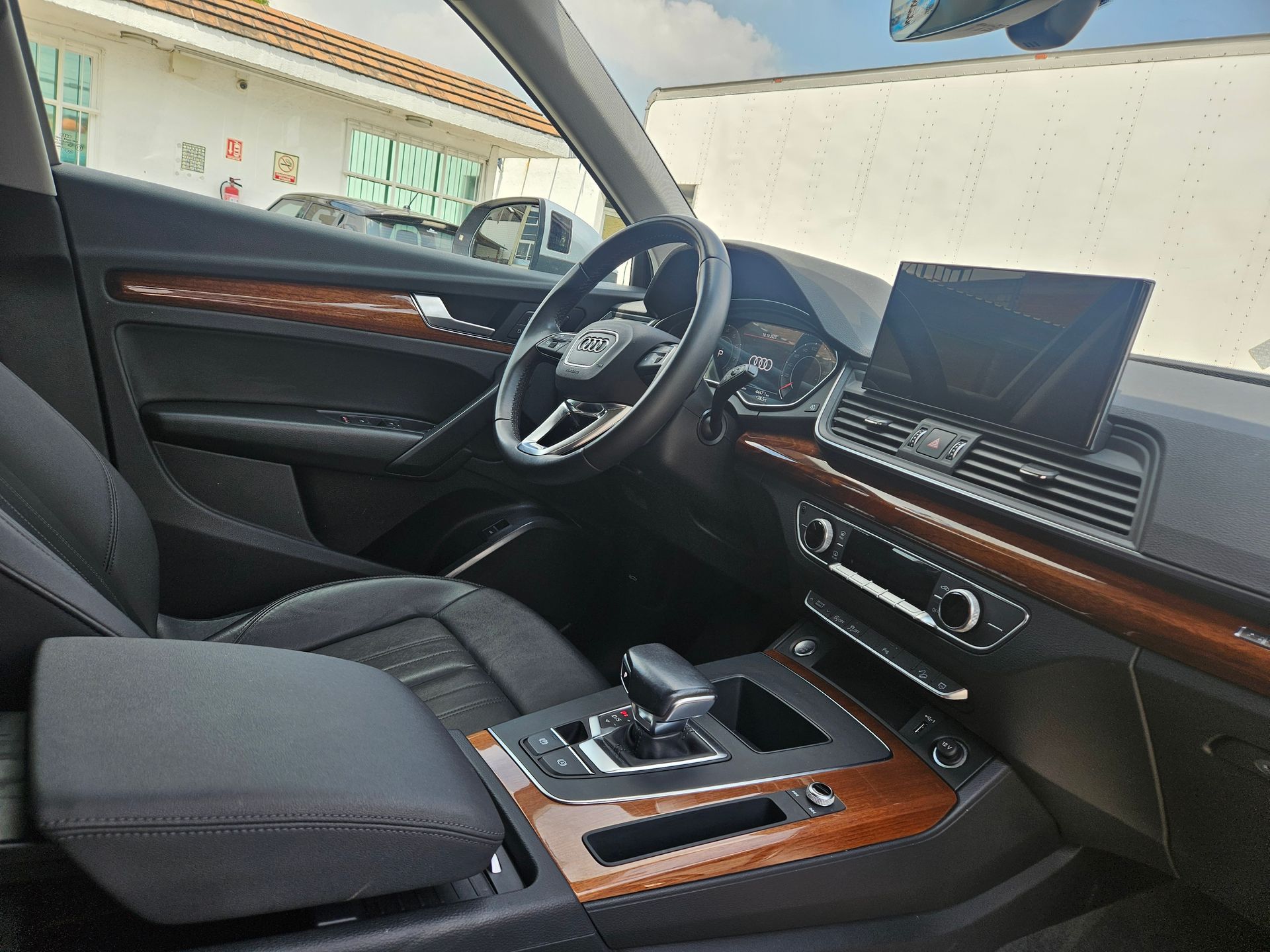 Vista interior de un Audi Q5; asientos de cuero negro, molduras de madera, volante, pantalla de infoentretenimiento y palanca de cambios.