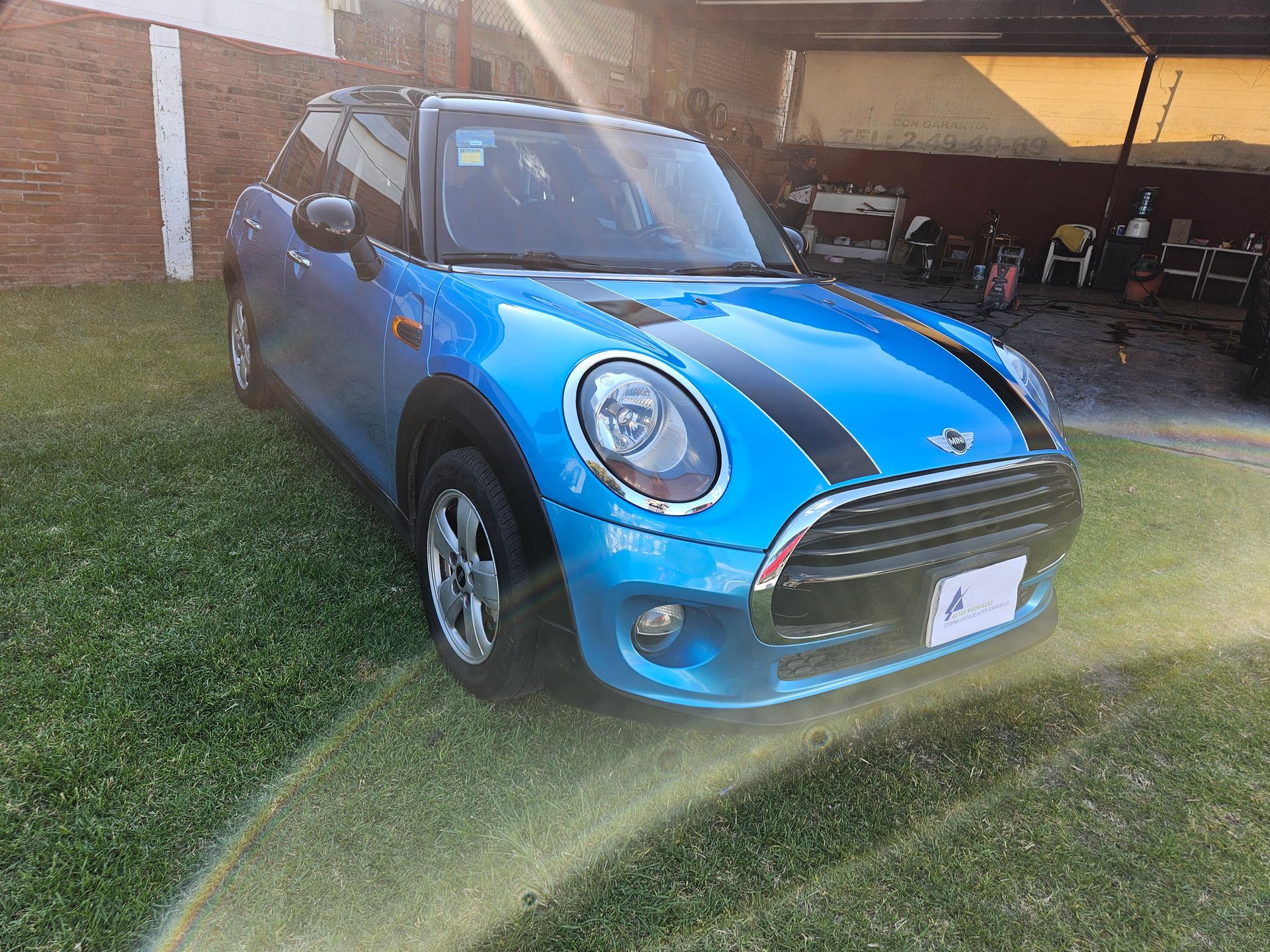 Coche Mini Cooper azul aparcado sobre el césped, rayas negras en el capó.