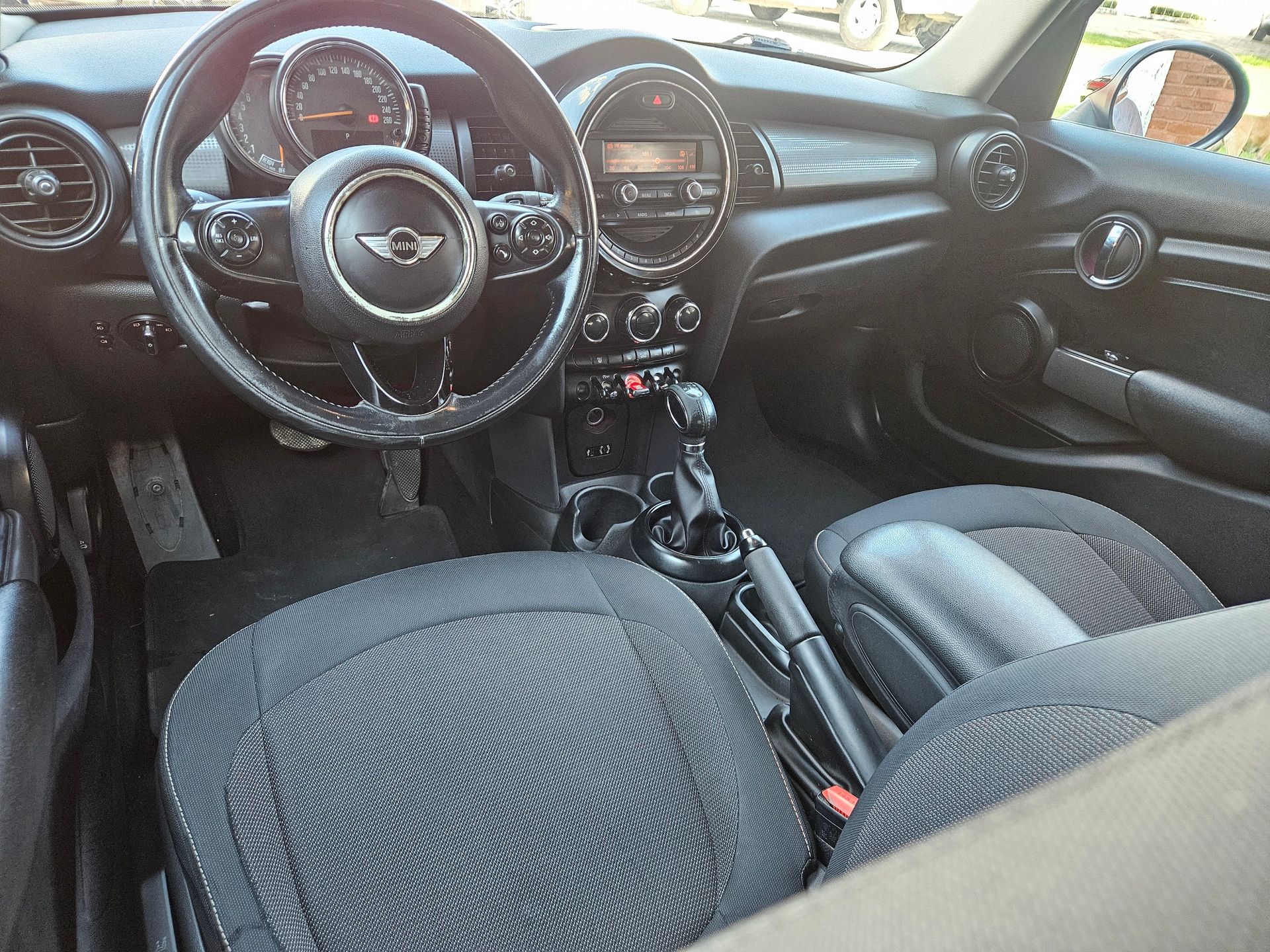 Vista interior de un Mini Cooper; tablero, volante, asientos y consola negros.