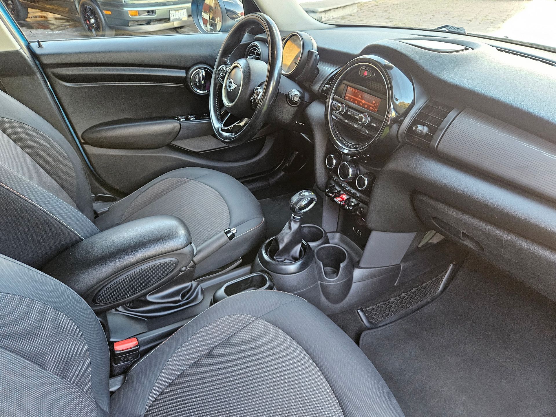 Interior de un Mini Cooper, asientos y salpicadero negros, volante visible.