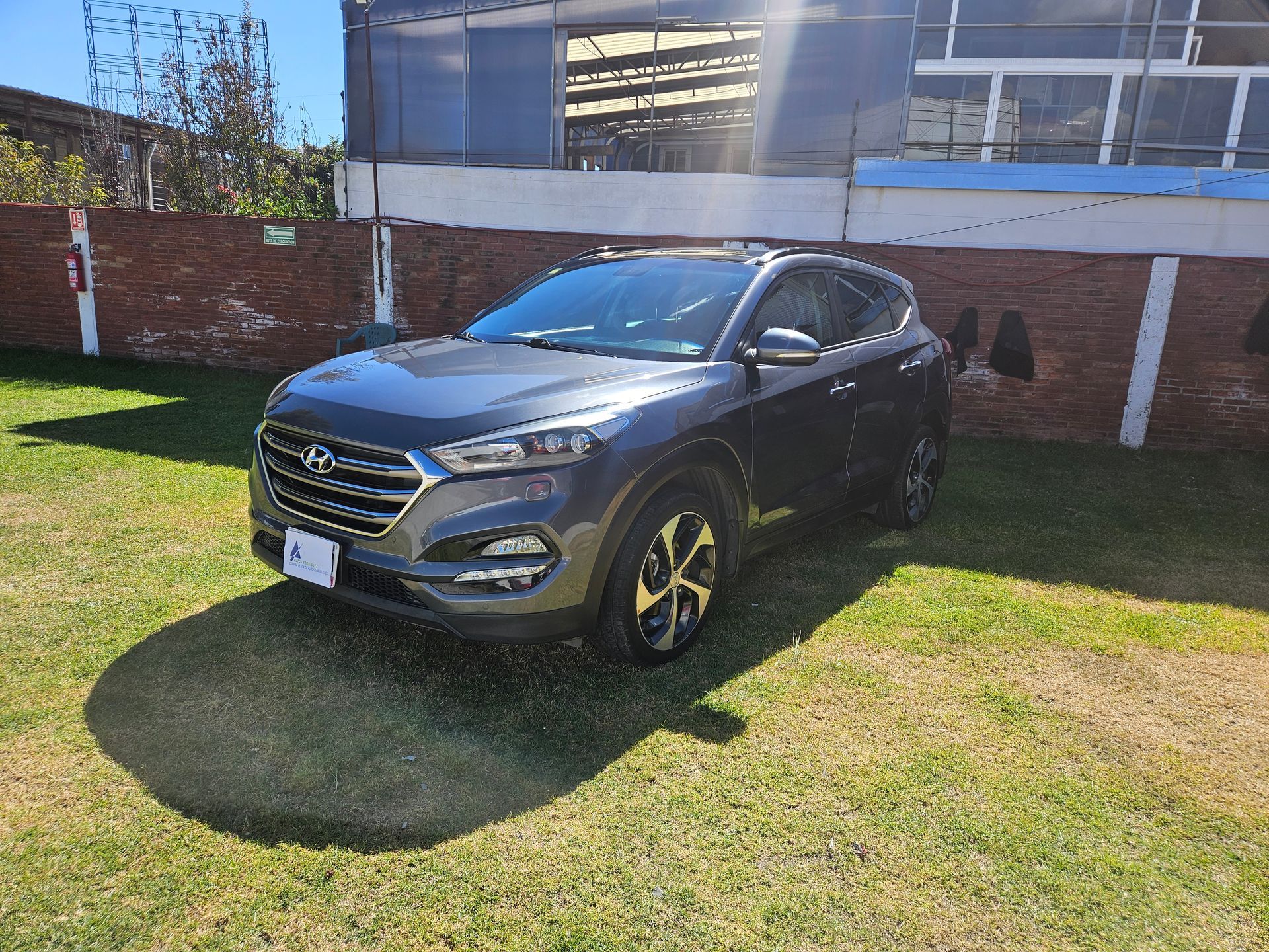 SUV Hyundai Tucson gris oscuro estacionado en una zona cubierta de hierba, día soleado.