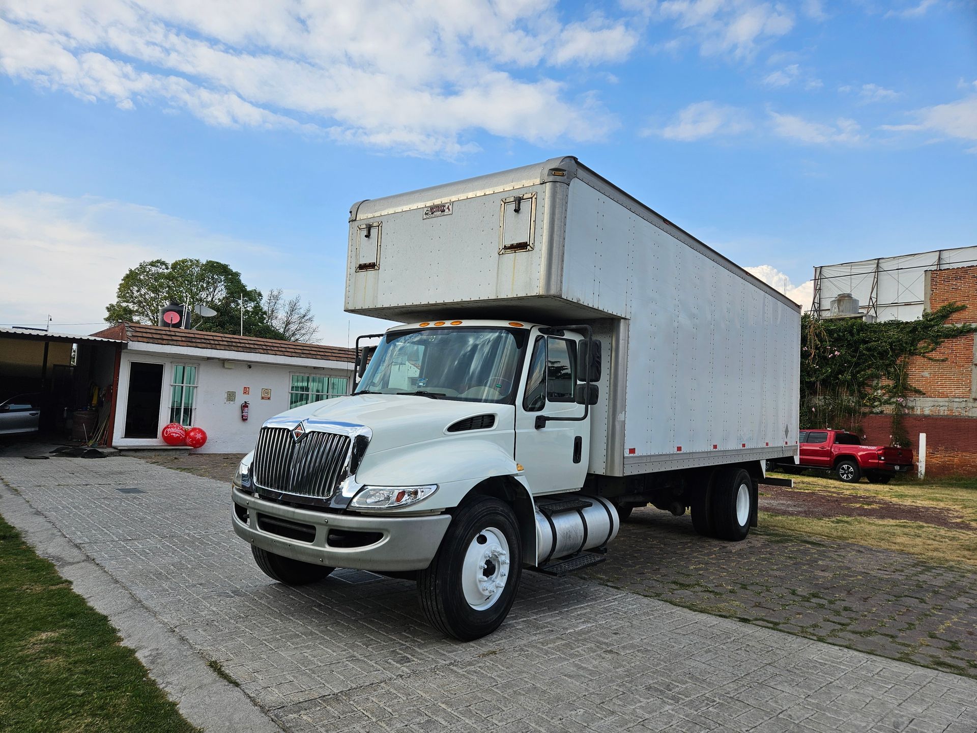 Camión de caja blanca estacionado en la entrada, entorno rural.