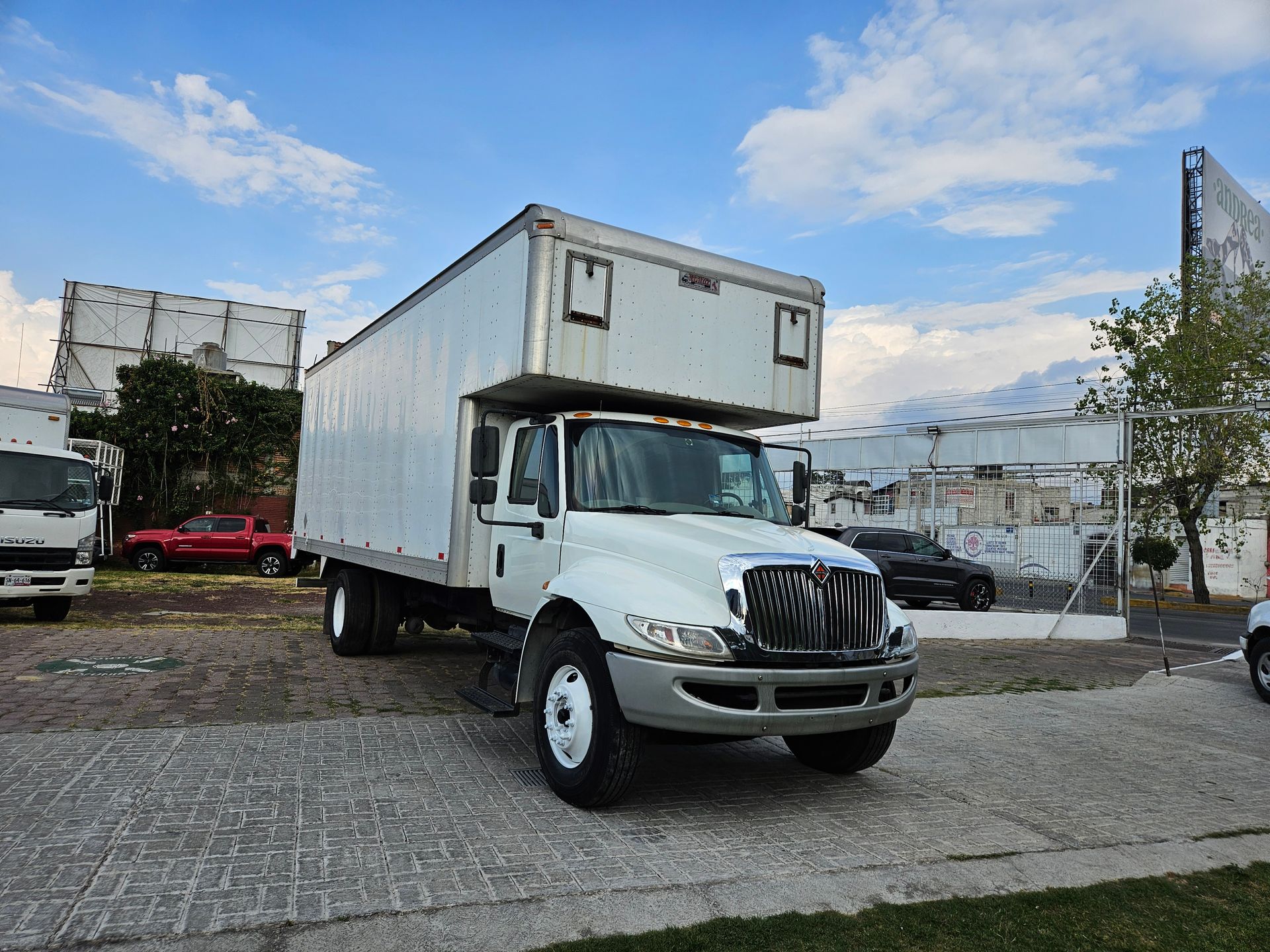 Camión de caja blanca estacionado en un lote pavimentado con un cielo parcialmente nublado en el fondo.