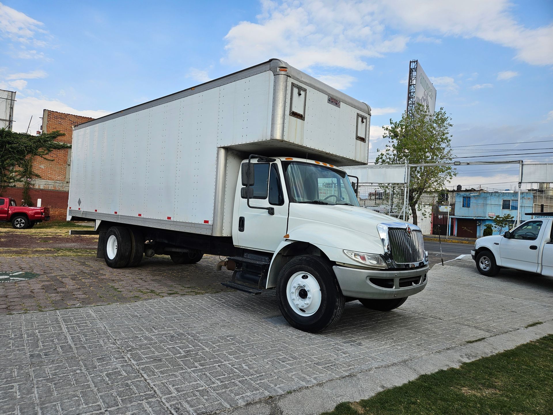 Un camión blanco estacionado sobre adoquines grises. Al fondo se ven edificios y el cielo.