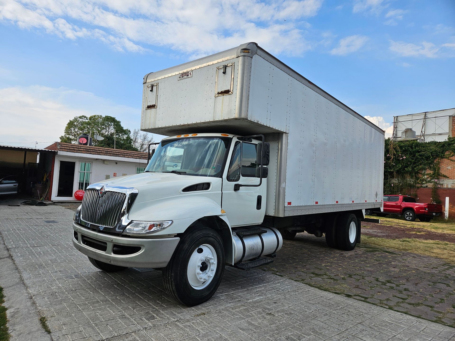 Camión de caja blanca estacionado en una zona pavimentada, bajo un cielo azul.
