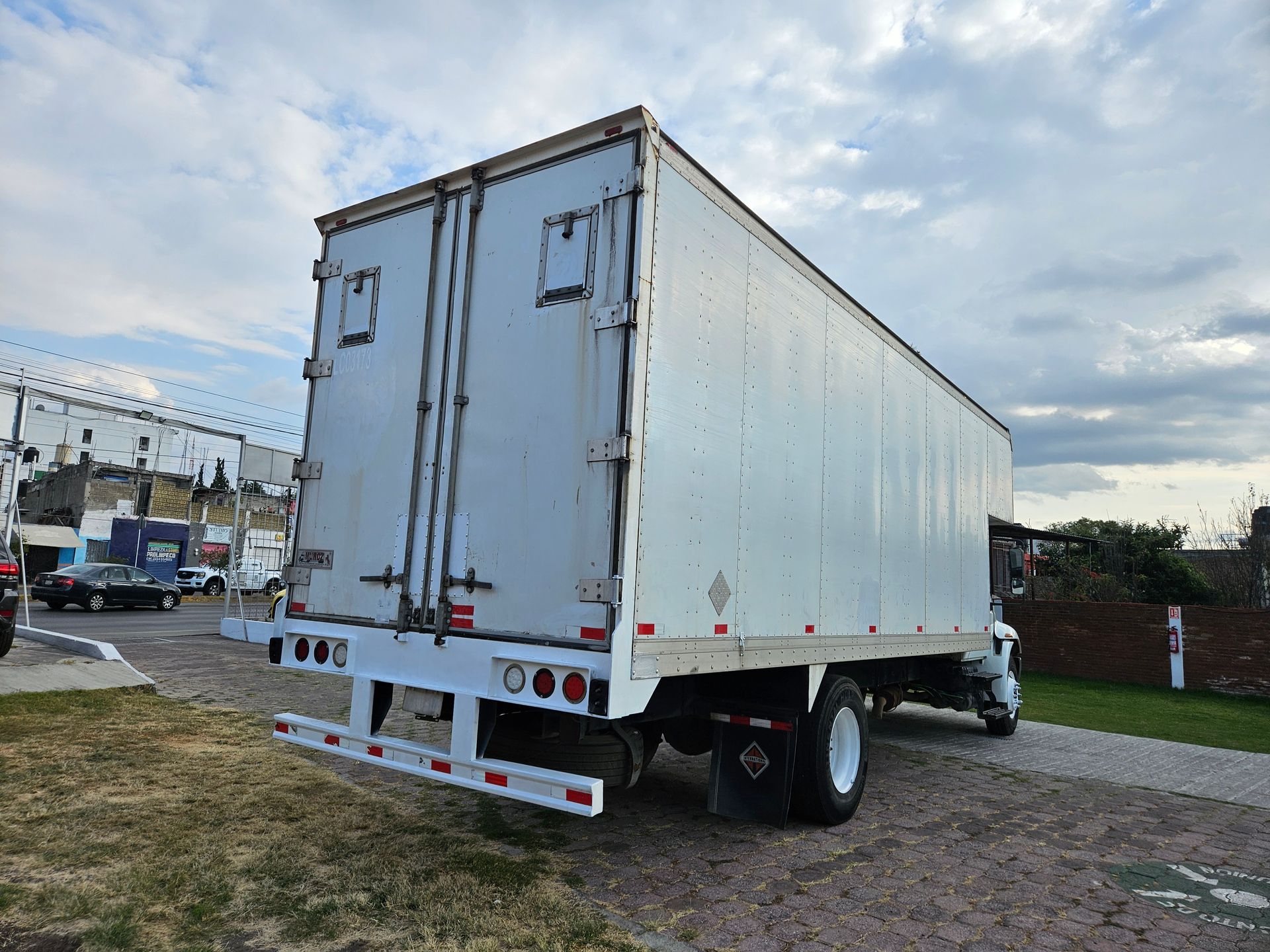 Vista trasera de un camión blanco con cielo nublado. El camión está estacionado sobre grava.