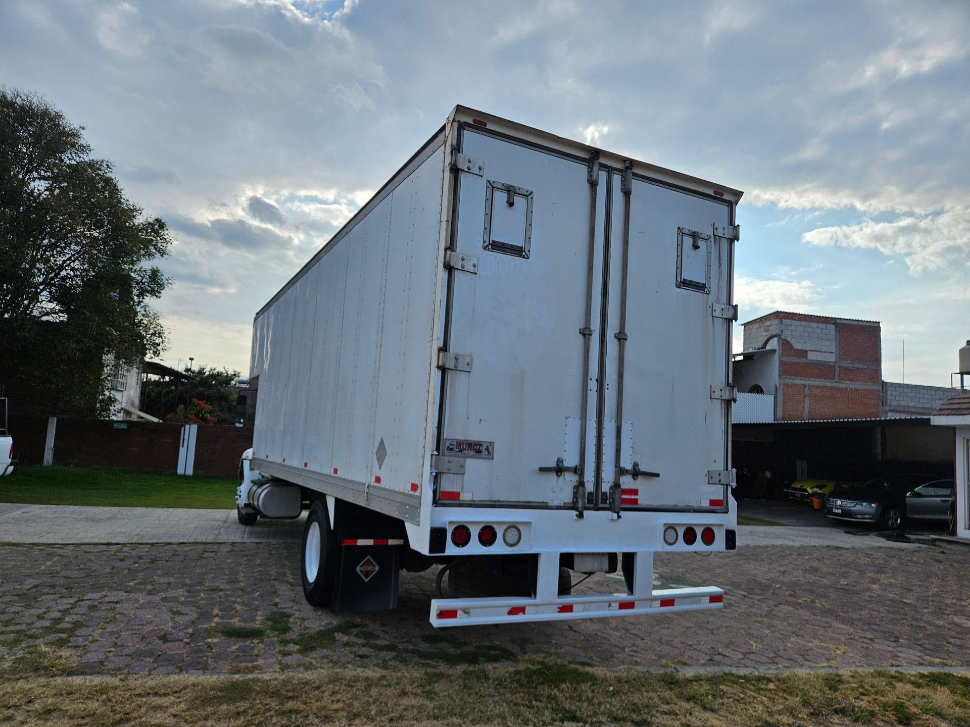Remolque semirremolque blanco, vista trasera, estacionado al aire libre bajo cielo nublado.