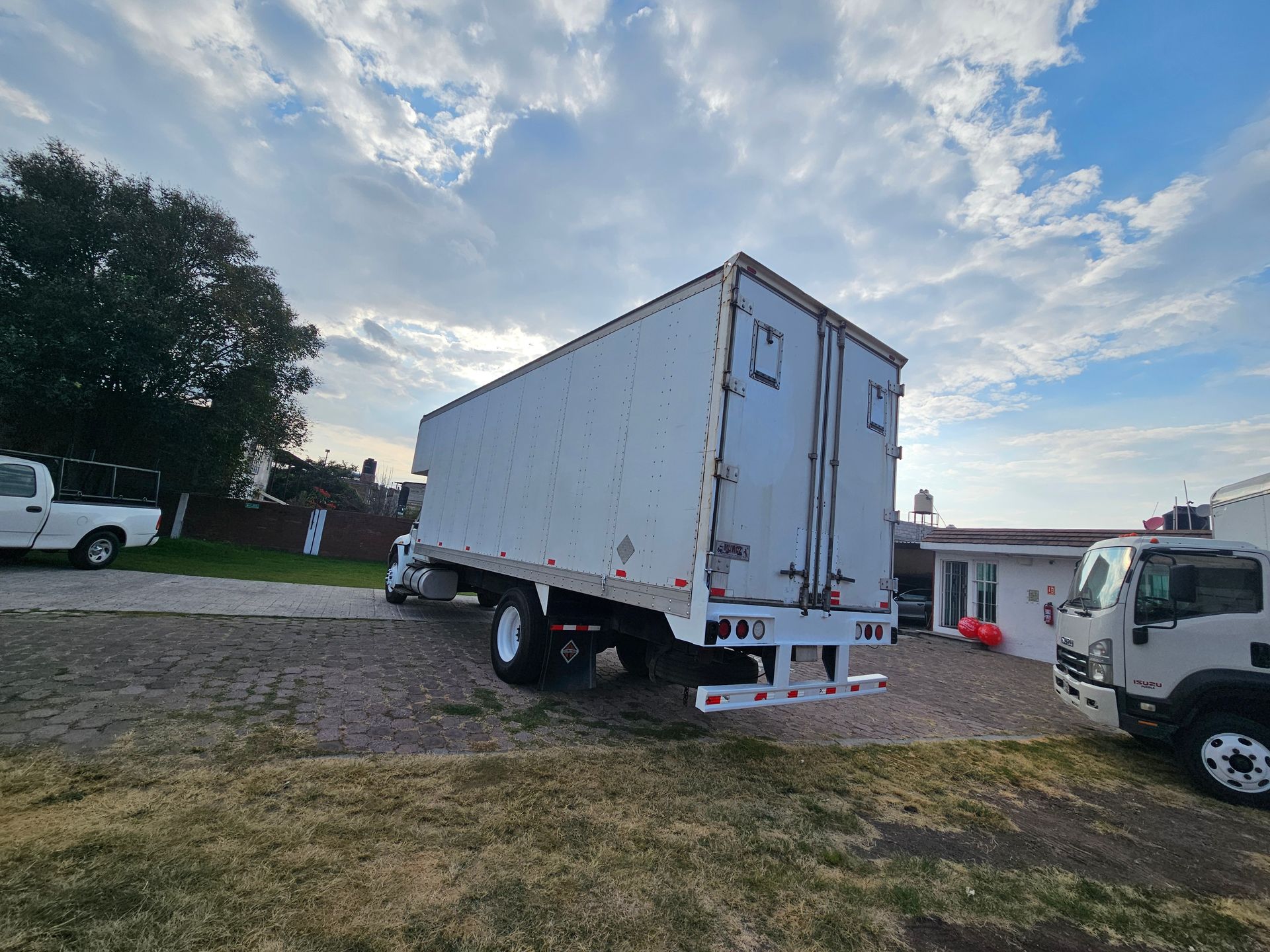 Camión de caja blanca en un lote de grava bajo un cielo nublado.