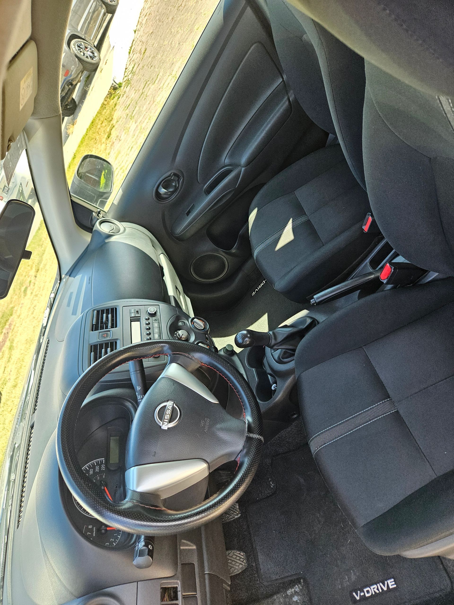Interior de un coche Nissan: volante, tablero, asientos negros.