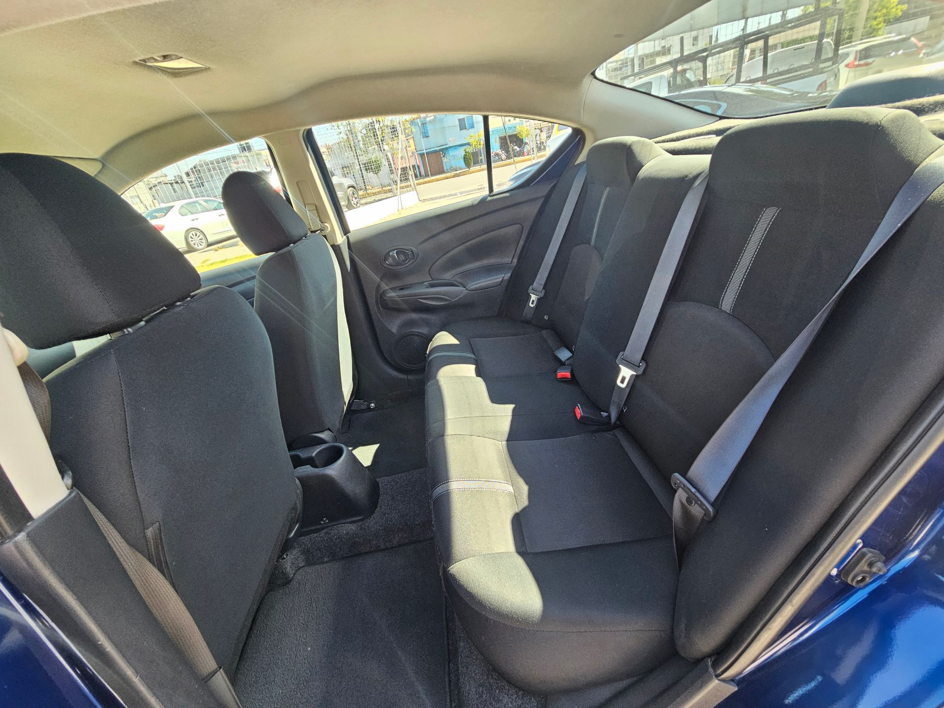 Vista interior de un coche azul. Asientos y cinturones de seguridad negros, y un vistazo al exterior a través de las ventanas.