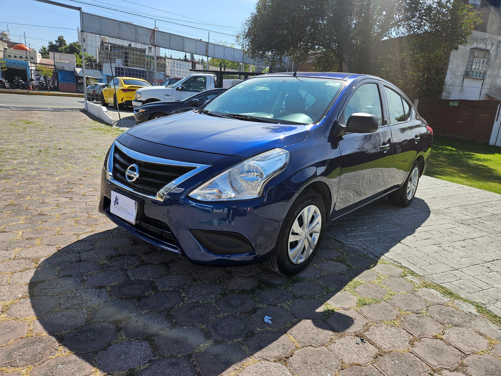 Un sedán Nissan Versa azul estacionado en un lote pavimentado en un día soleado.