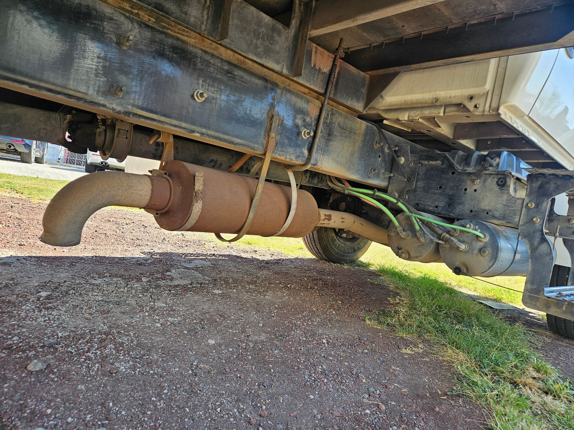 Parte inferior de un camión, que muestra un silenciador de escape oxidado y componentes relacionados.