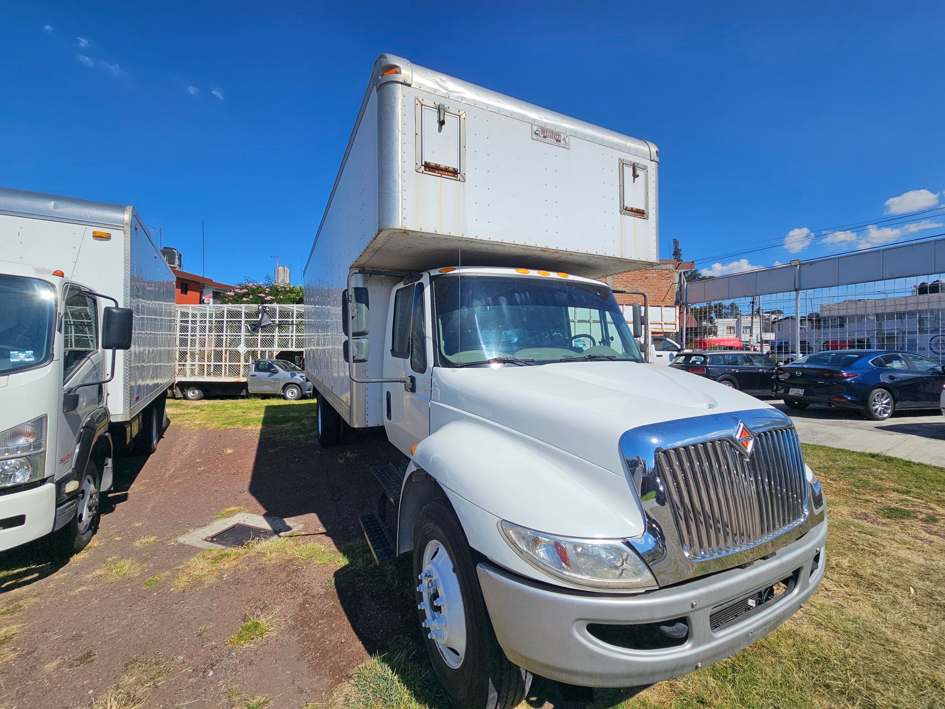 Camión de caja blanca estacionado sobre césped, fondo de cielo azul.