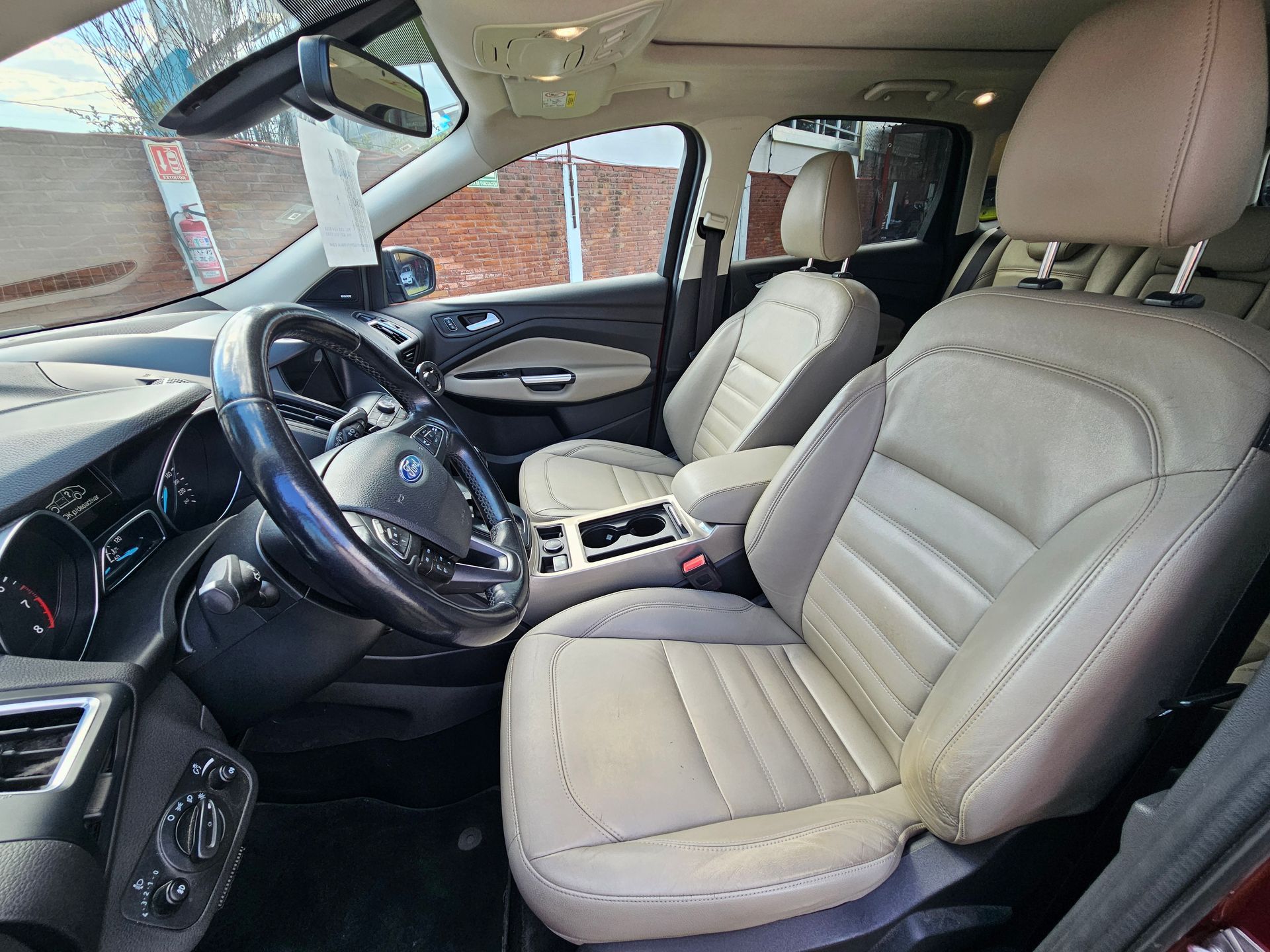 Interior color beige de un Ford Escape con asientos de cuero beige y volante negro.