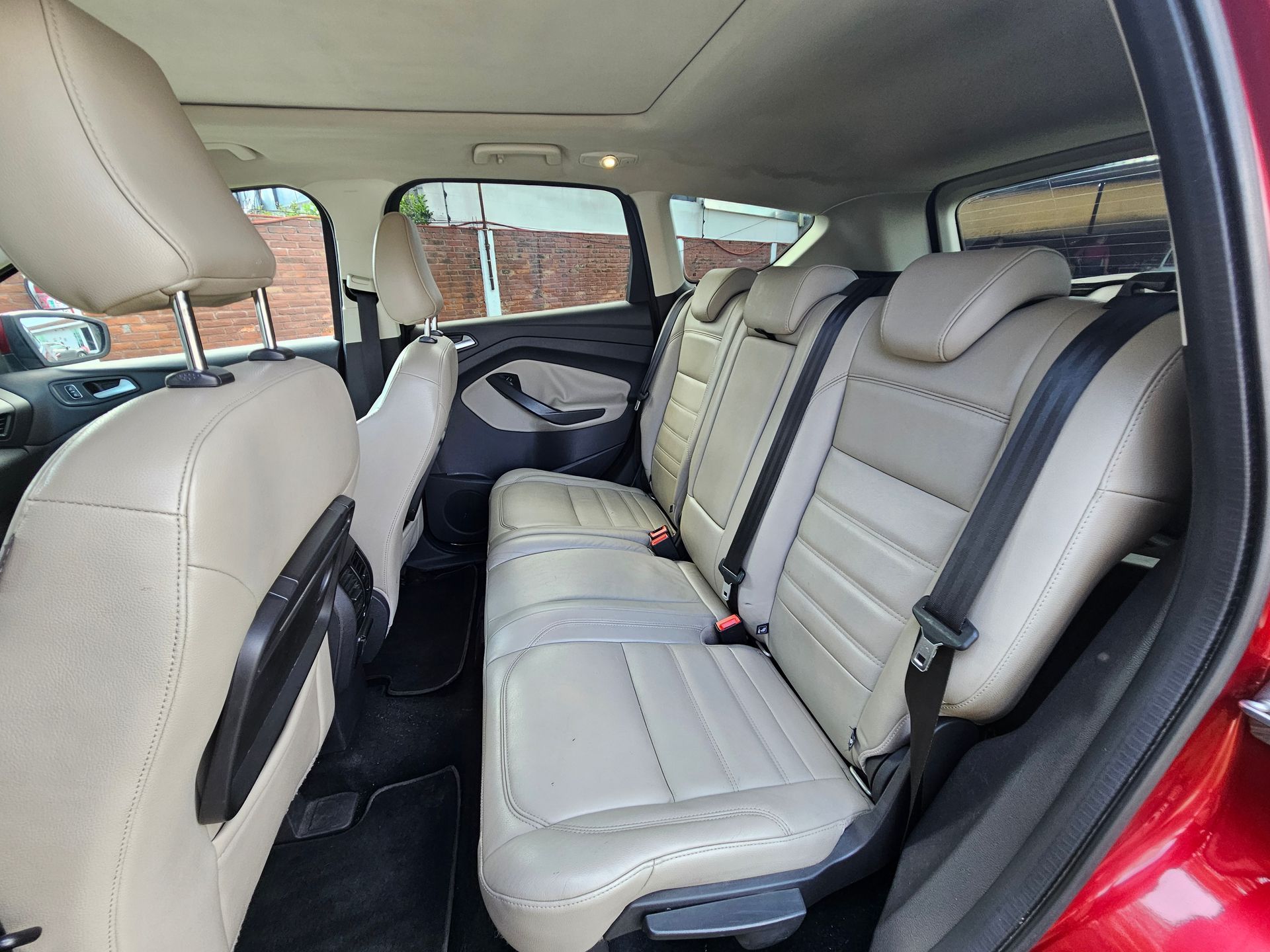 Vista interior de un SUV Ford rojo con asientos de cuero beige y techo corredizo.