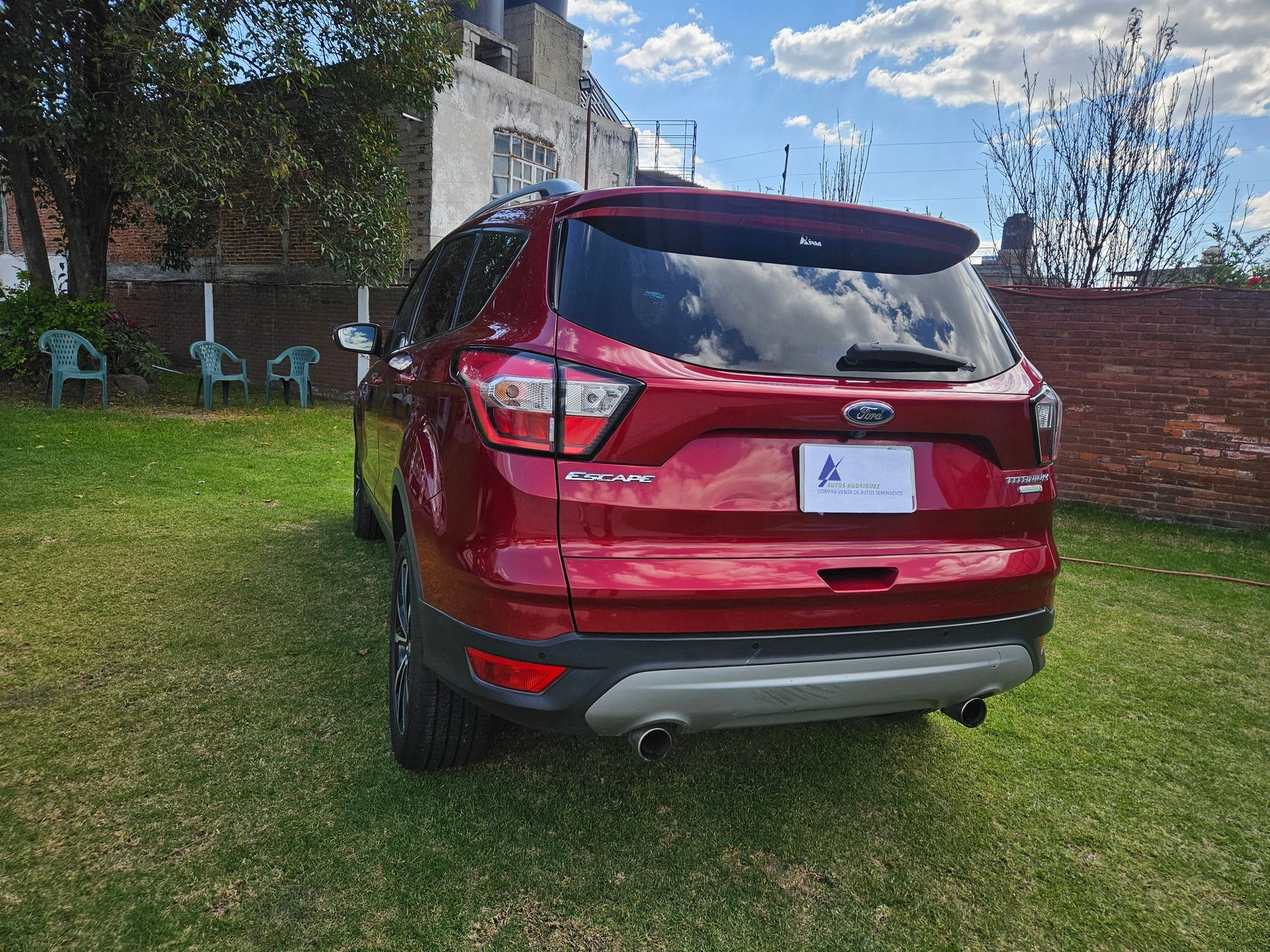 Ford Escape SUV roja estacionada sobre césped, vista en ángulo. Se ven luces traseras, alerón y parachoques gris.