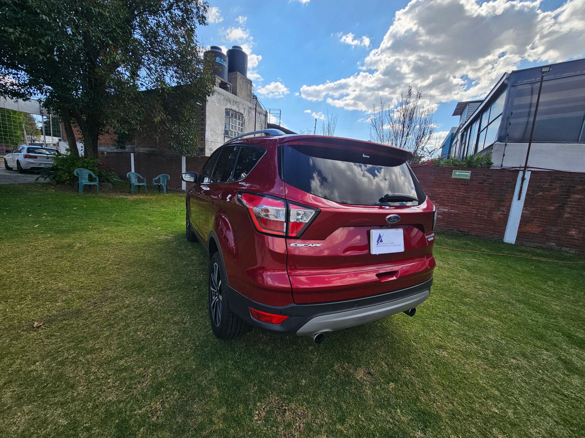 SUV rojo estacionado en el césped con un edificio blanco y un cielo azul en el fondo.